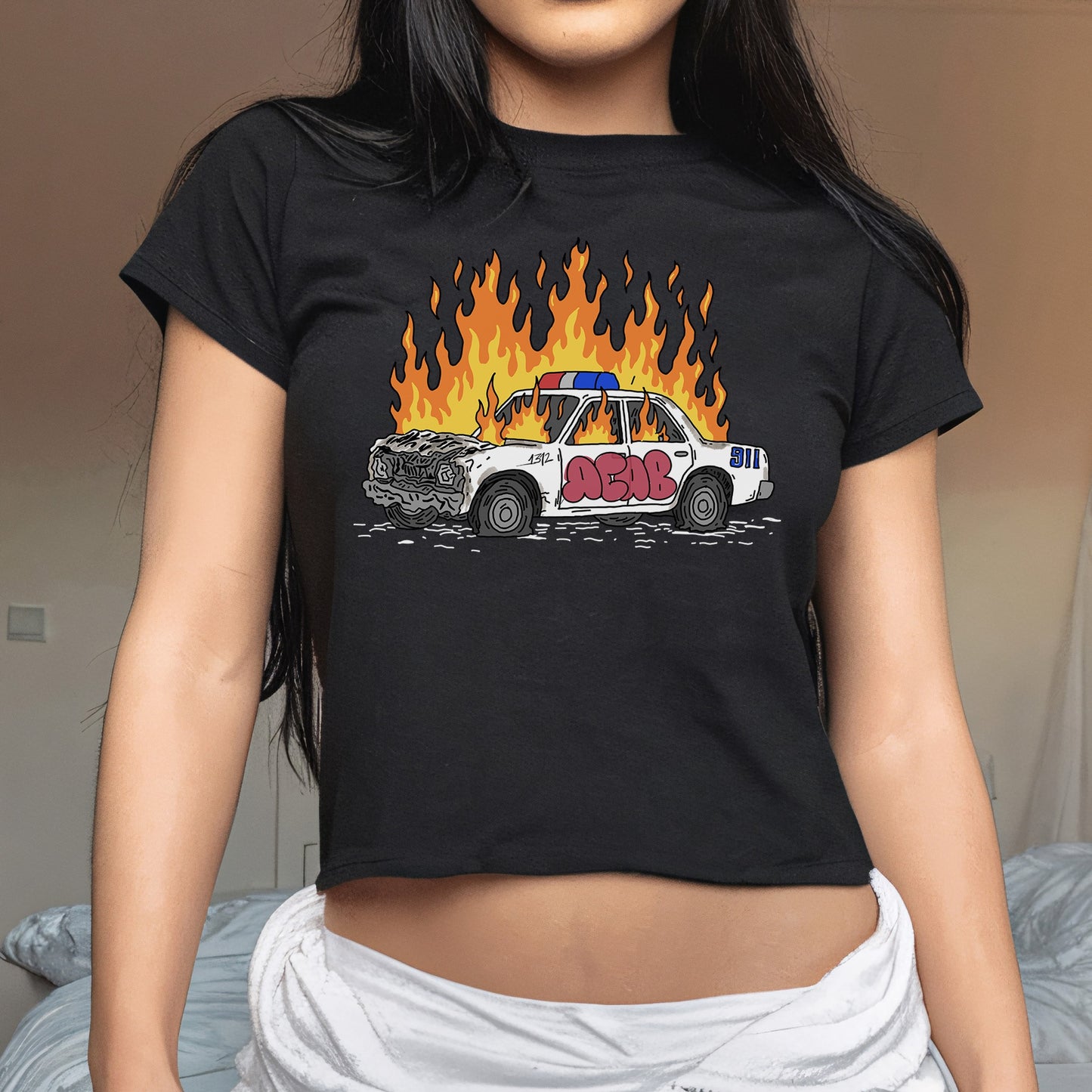 ACAB Police Car Women's Baby Tee features a cartoon wrecked police car in flames with graffiti ACAB, embodying a bold, rebellious statement on a black, slightly cropped T-shirt.