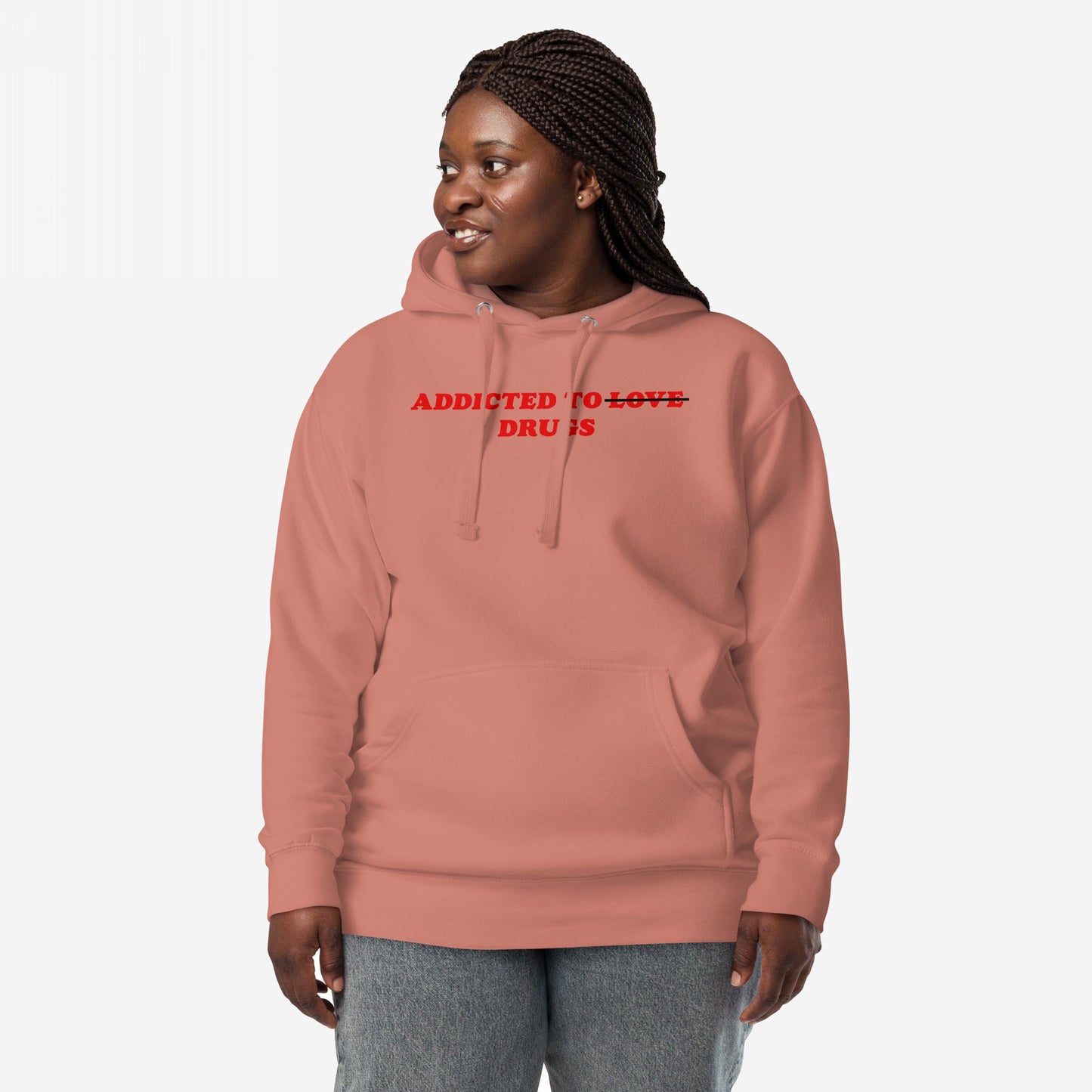 Person in a muted rose-pink Addicted To Love / Drugs Hoodie & Sweatshirt, featuring bold red text with Love crossed out, paired with light-wash jeans, embodying raw, reflective streetwear.