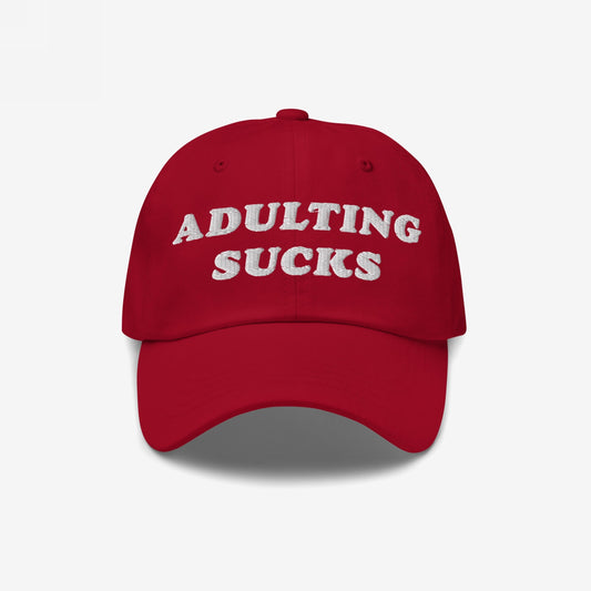 Red baseball cap with ADULTING SUCKS embroidered in bold white letters, capturing a vintage-inspired style perfect for expressing relatable frustrations with adult life. Ideal for casual wear and gifting.
