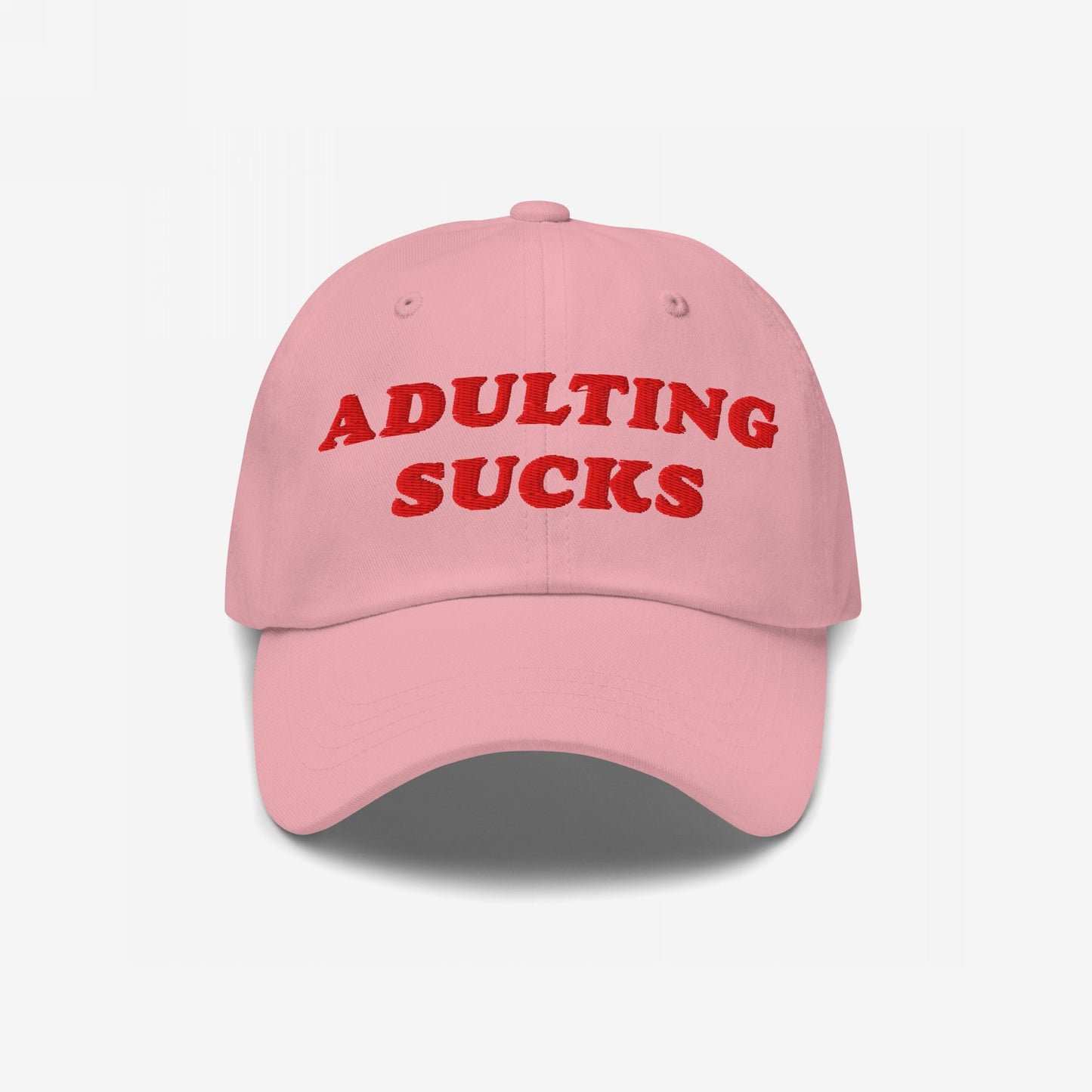 Light pink baseball cap with ADULTING SUCKS in bold red embroidery, expressing a humorous take on life's challenges. The cap embodies a candid and relatable message about adulthood's struggles.