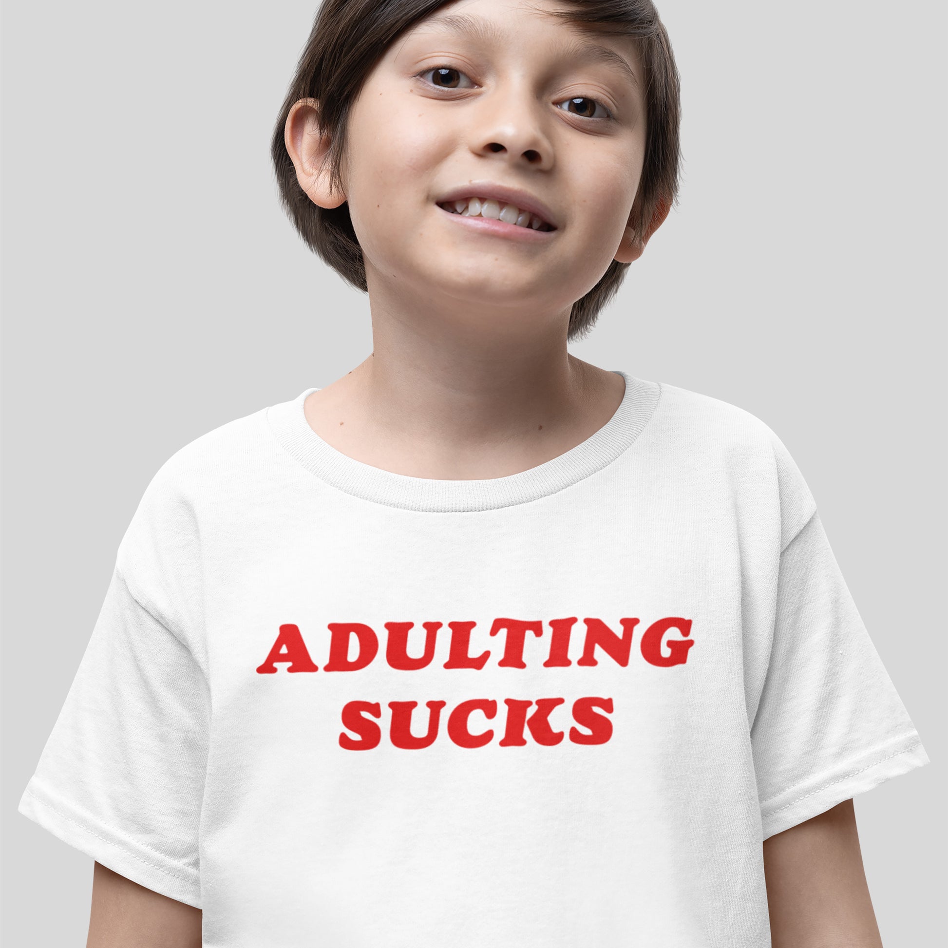 Young boy wearing an Adulting Sucks T-shirt with bold red lettering, humorously capturing the challenges of grown-up life with a casual, expressive design ideal for all ages.