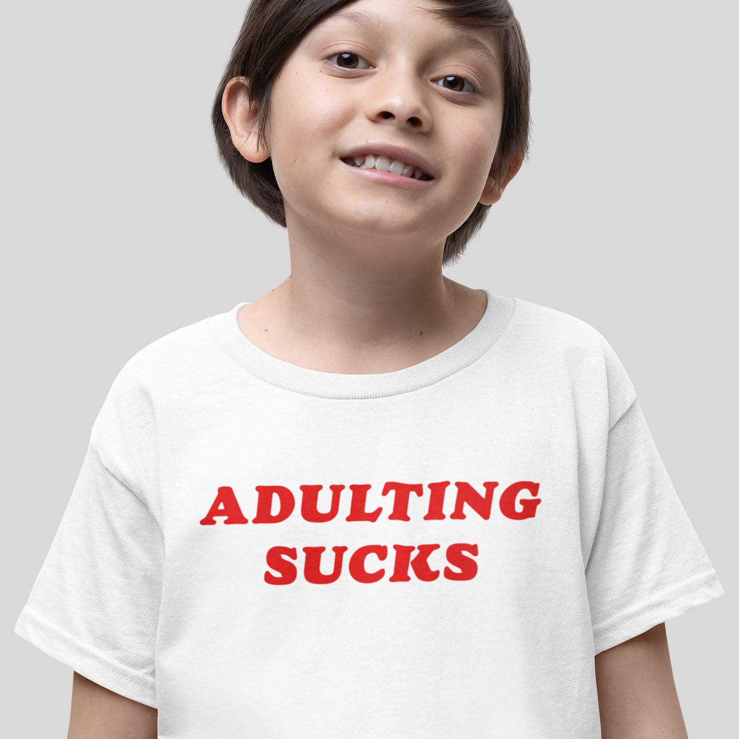 Young child wearing the Adulting Sucks T-shirt in bold red letters, conveying a playful resistance to adult responsibilities. The shirt's retro style adds a nostalgic touch to this candid statement piece.