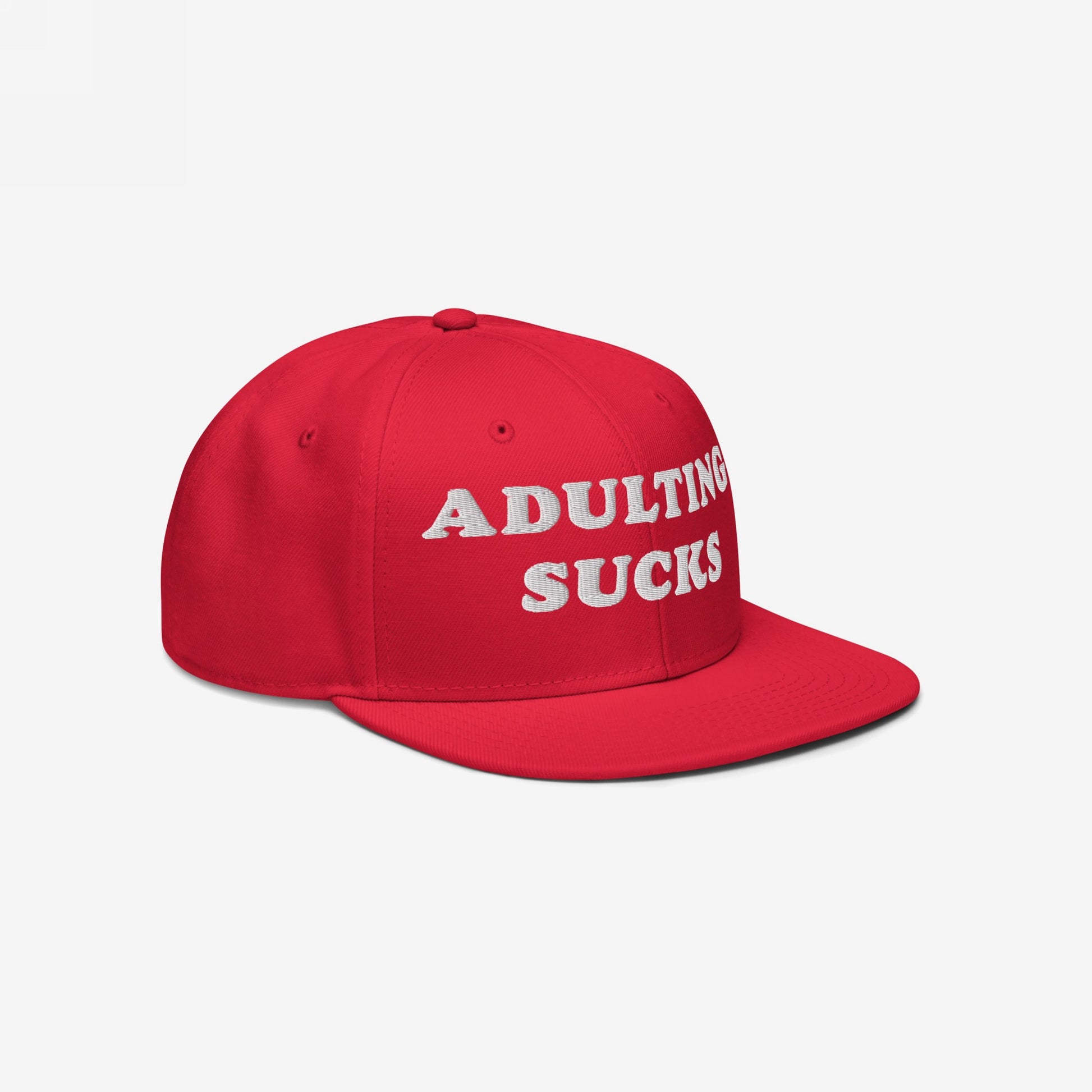 Red flat-brim snapback cap with “ADULTING SUCKS” embroidered in white, reflecting a relatable sentiment for adults. Ideal for casual wear, this hat is perfect for expressing individuality and humor.