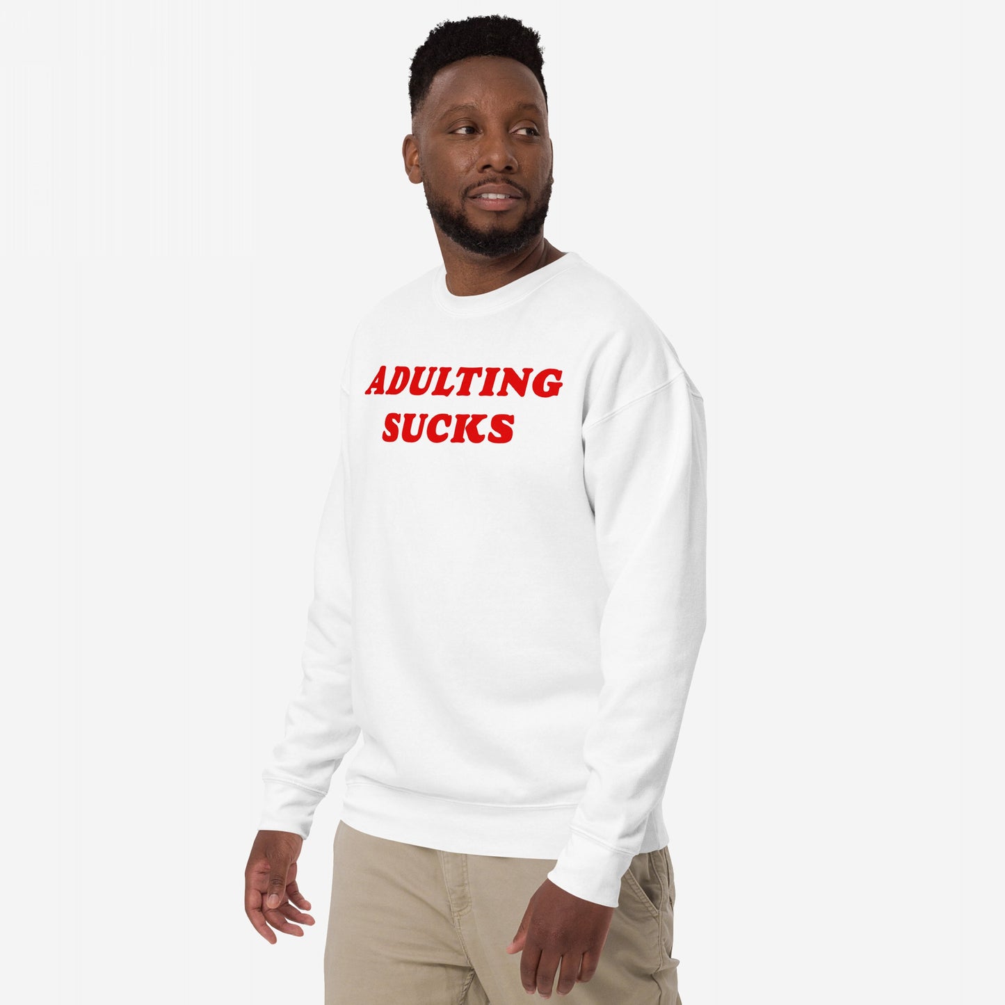 Man in Adulting Sucks crewneck sweatshirt, featuring bold red text, expressing humor in everyday challenges. He's paired it with light pants, embodying the relatable theme of grown-up burnout.