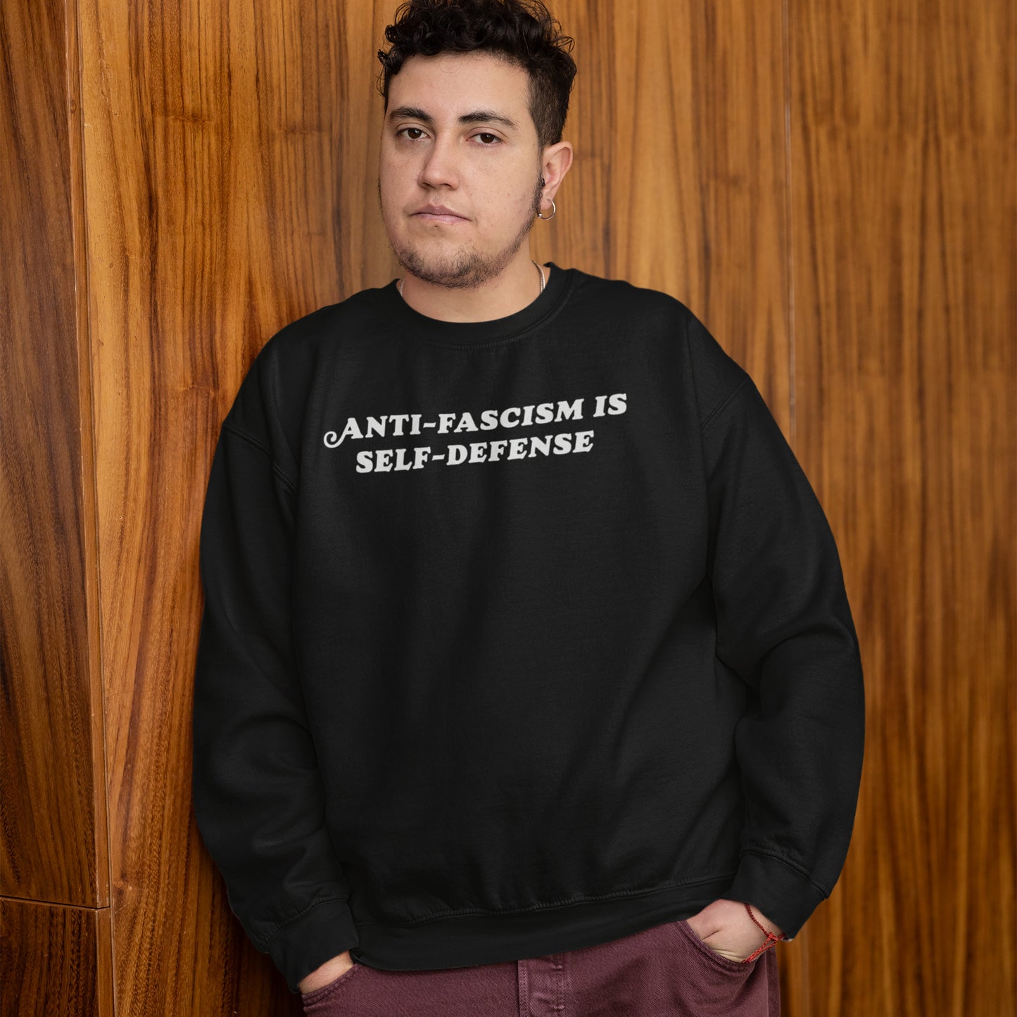 Person wearing Anti Fascism Is Self Defense Shirt with bold text, standing confidently. The black sweatshirt conveys a strong message of justice and resistance, aligning with values of activism and equality.