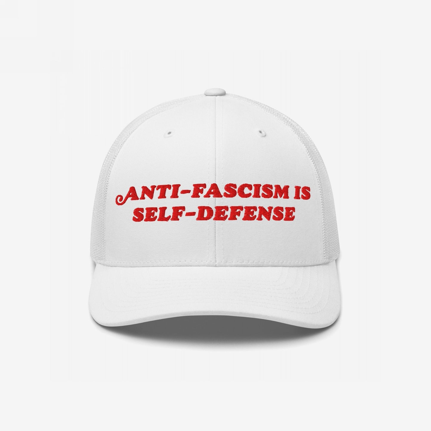 White mesh-back trucker hat with bold red embroidered text ANTI-FASCISM IS SELF-DEFENSE on the front, embodying a strong message of resistance and activism.