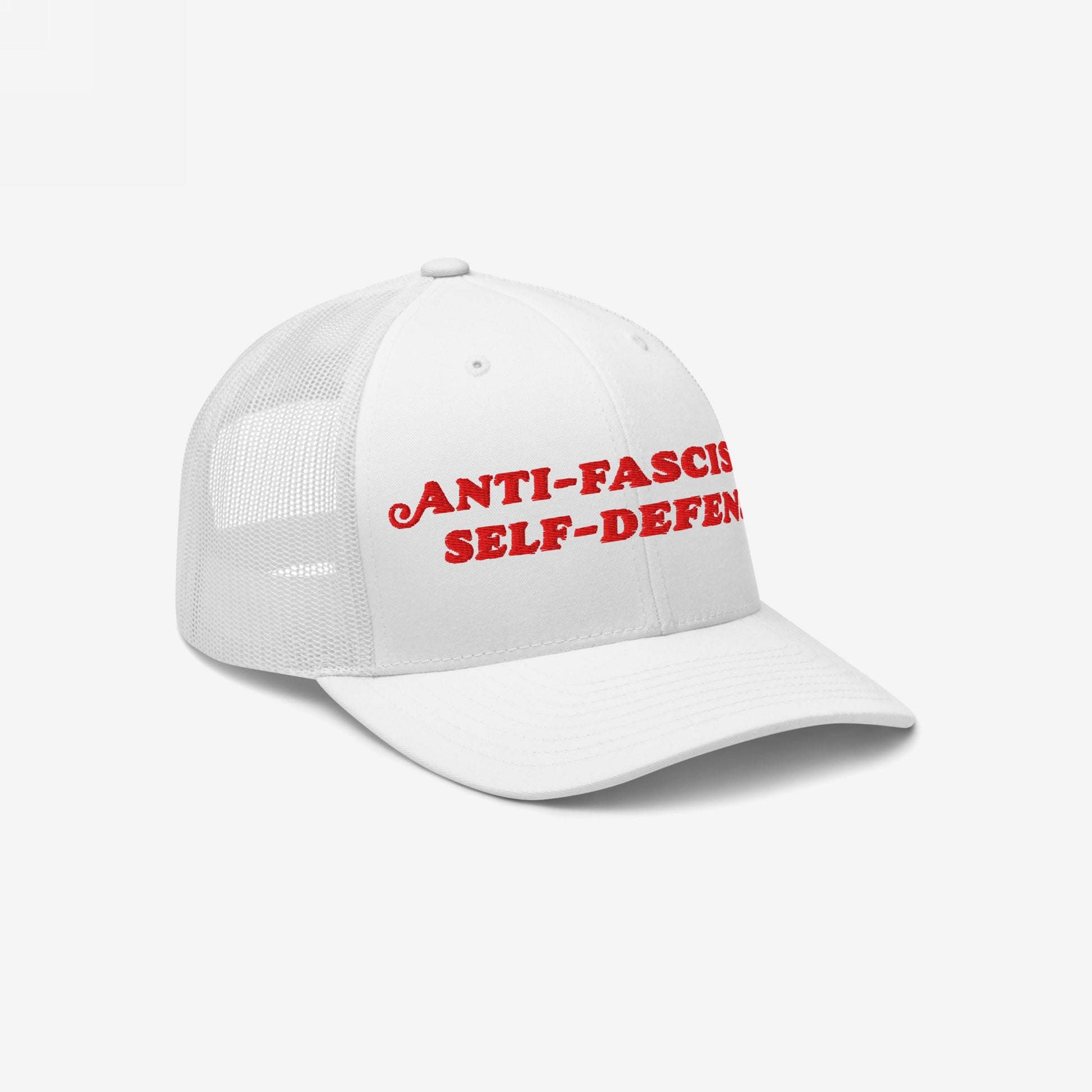 White trucker-style baseball cap with mesh back, featuring bold red ANTI-FASCIST SELF-DEFENCE embroidery. This Anti Fascism Is Self Defense Hat is designed for activists and human rights defenders.