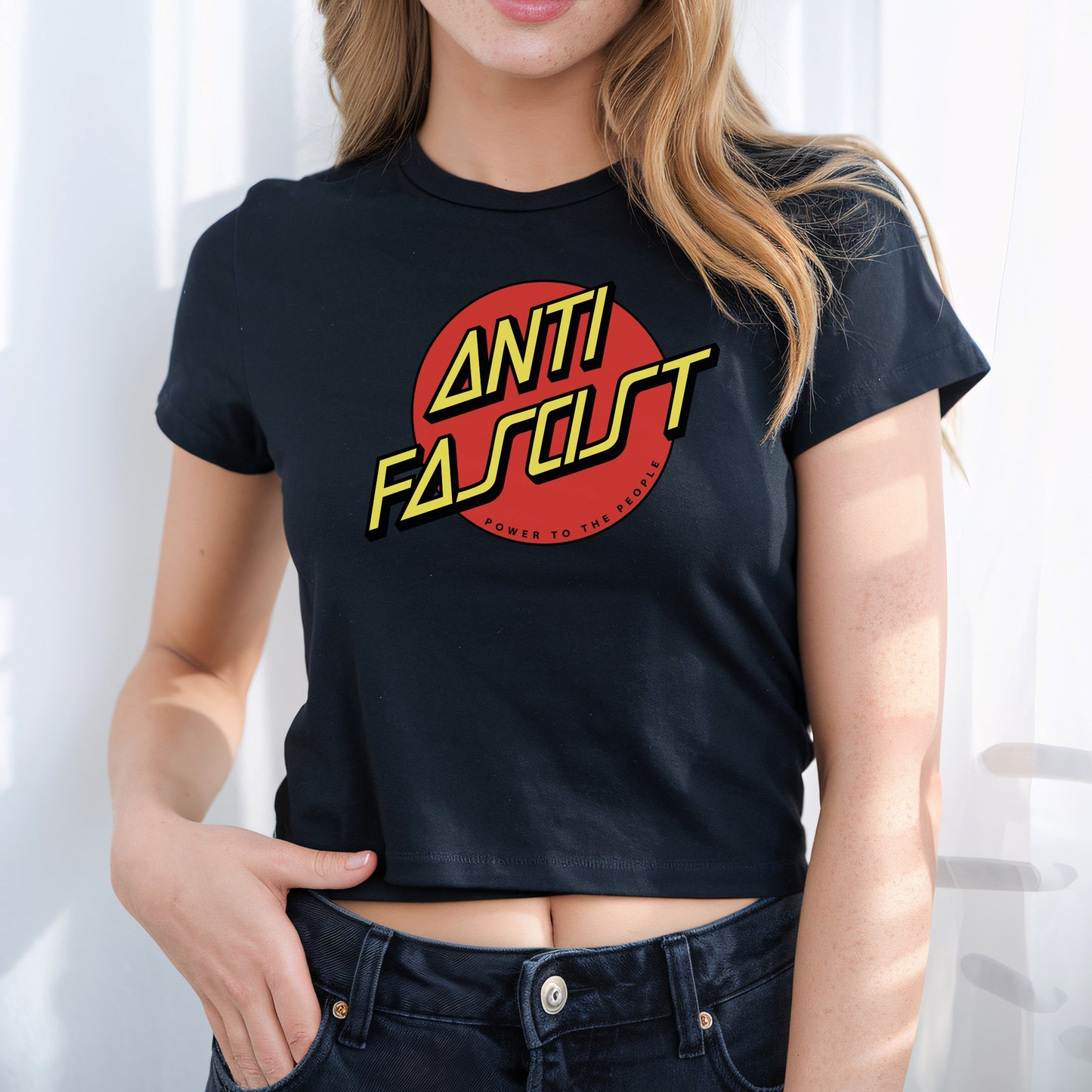 Person wearing the Anti-Fascist Women's Baby Tee, featuring a bold red circle and yellow text ANTI FASCIST with Power to the people, embodying defiant, anti-fascist style.