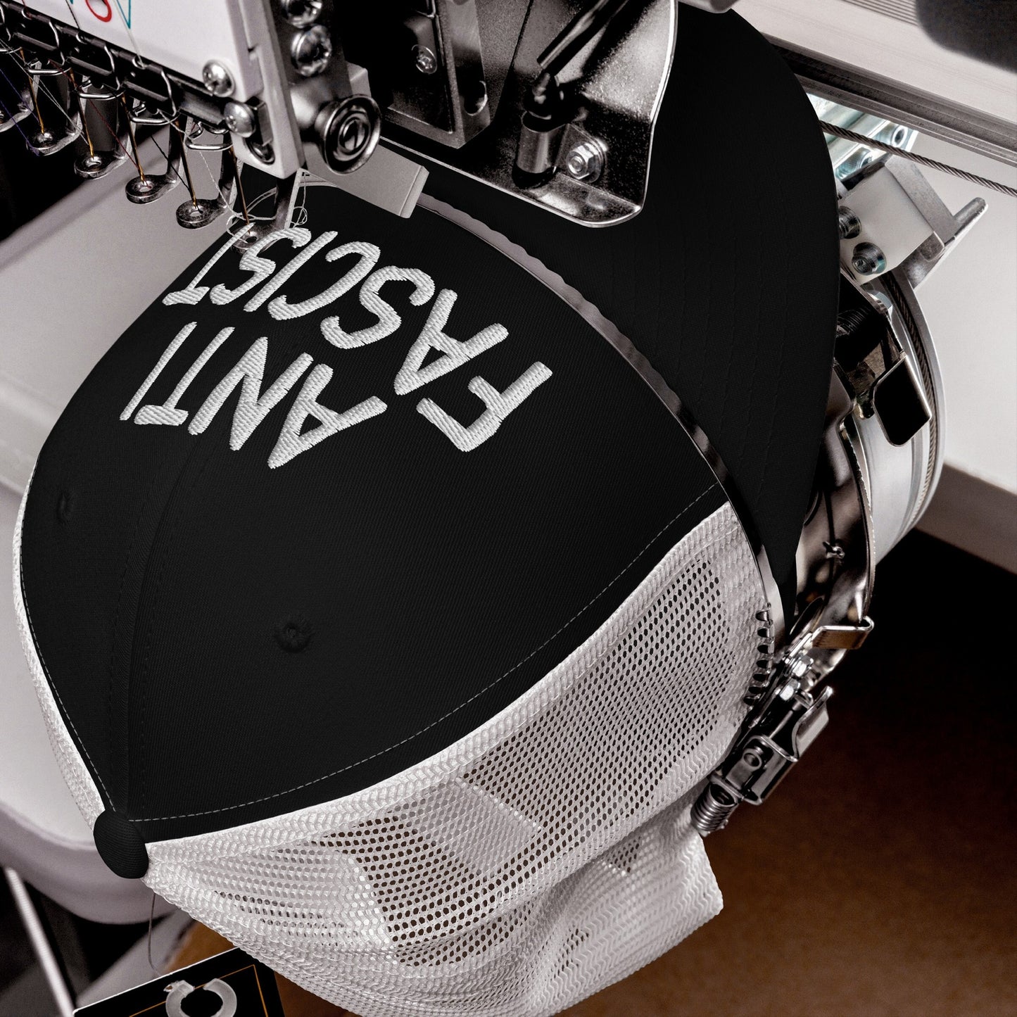 The Anti-Fascist Hat on an embroidery machine, displaying ANTI FASCIST in bold letters, represents a statement piece with a soft fit, ethically crafted for daily protest wear.