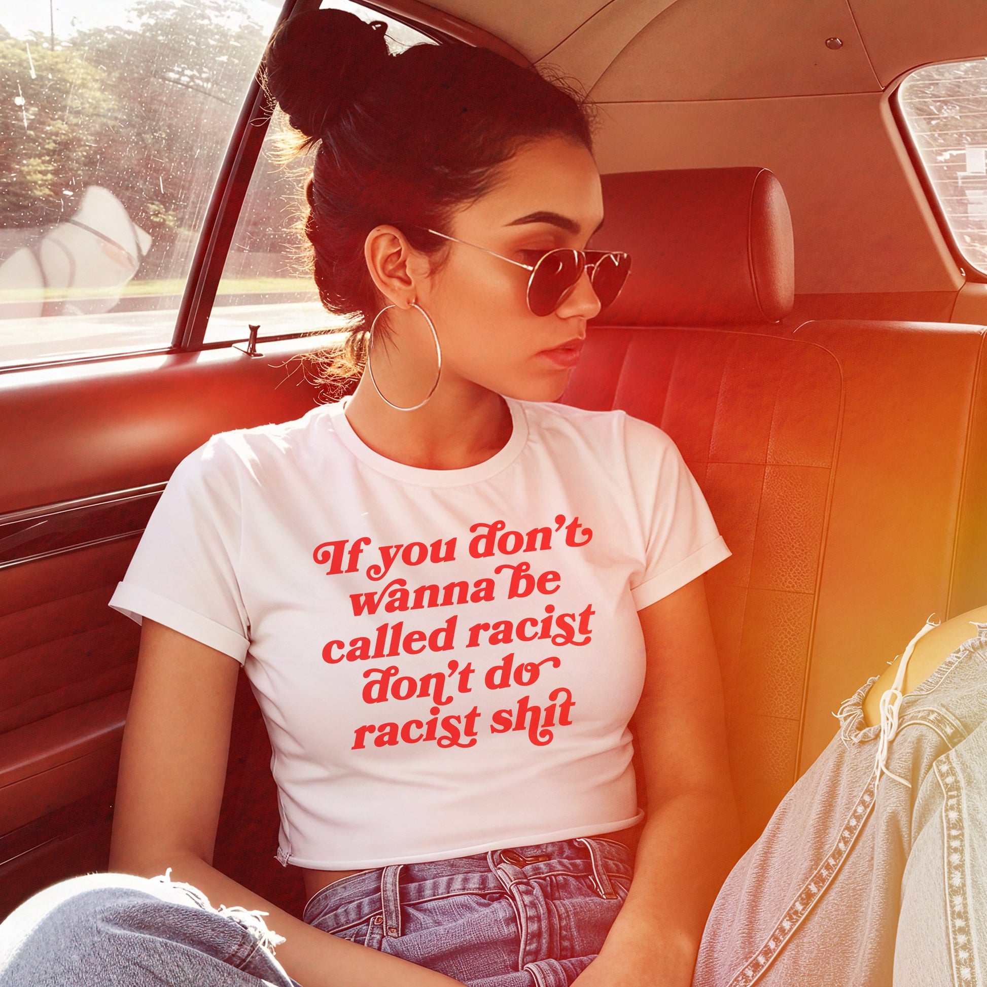 Anti-Racist Women's Baby Tee EU: A young woman in a car wears this bold, cropped T-shirt with a powerful anti-racist message, paired with aviator sunglasses and ripped jeans, projecting casual confidence.