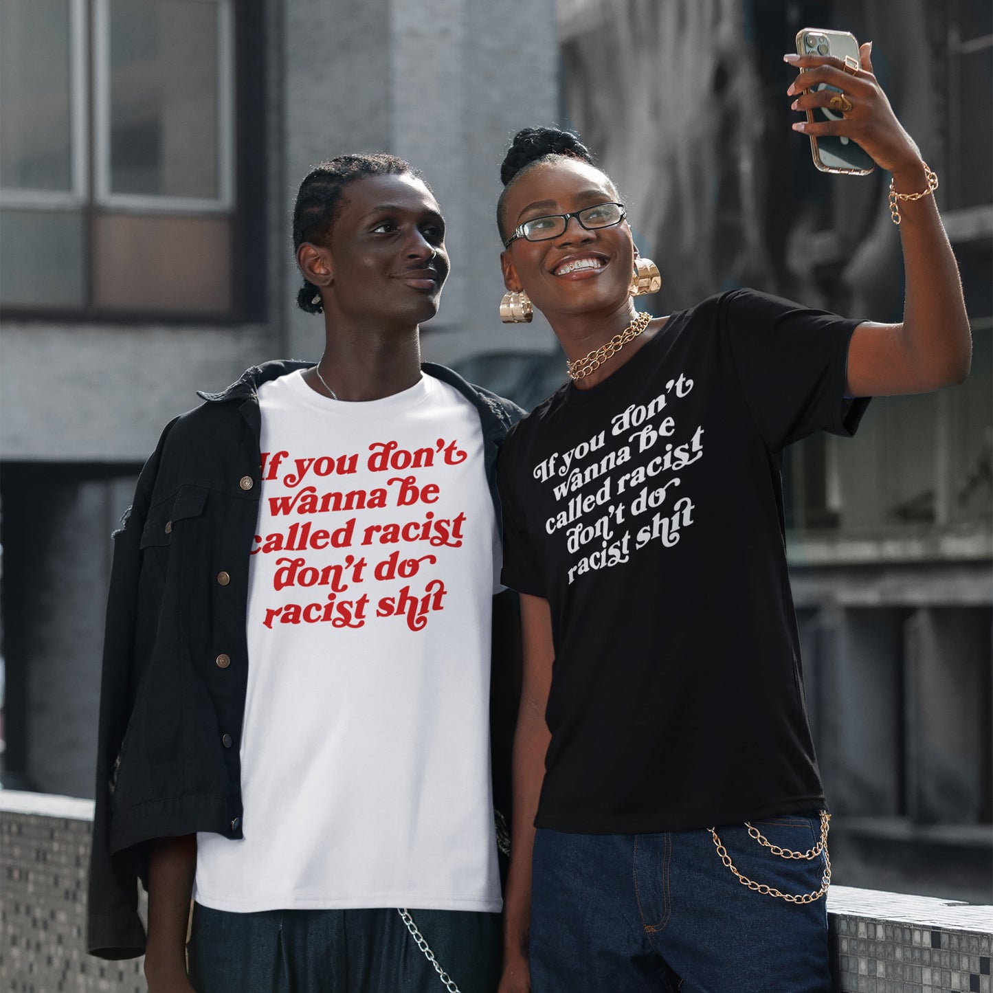 Two young adults wear the Anti-Racist Shirt with the slogan “If you don’t wanna be called racist don’t do racist shit,” embodying a bold, unapologetic stand against racism in a casual, urban setting.