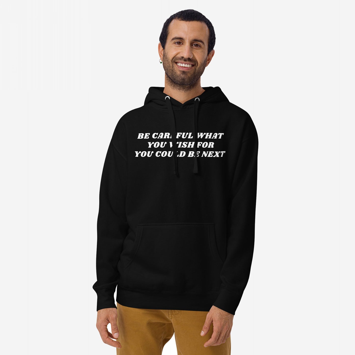 A man wears the Be Careful Hoodie & Sweatshirt with bold text challenging authority, reflecting a rebellious spirit. The black hoodie features a striking message, paired with tan pants against a neutral backdrop.