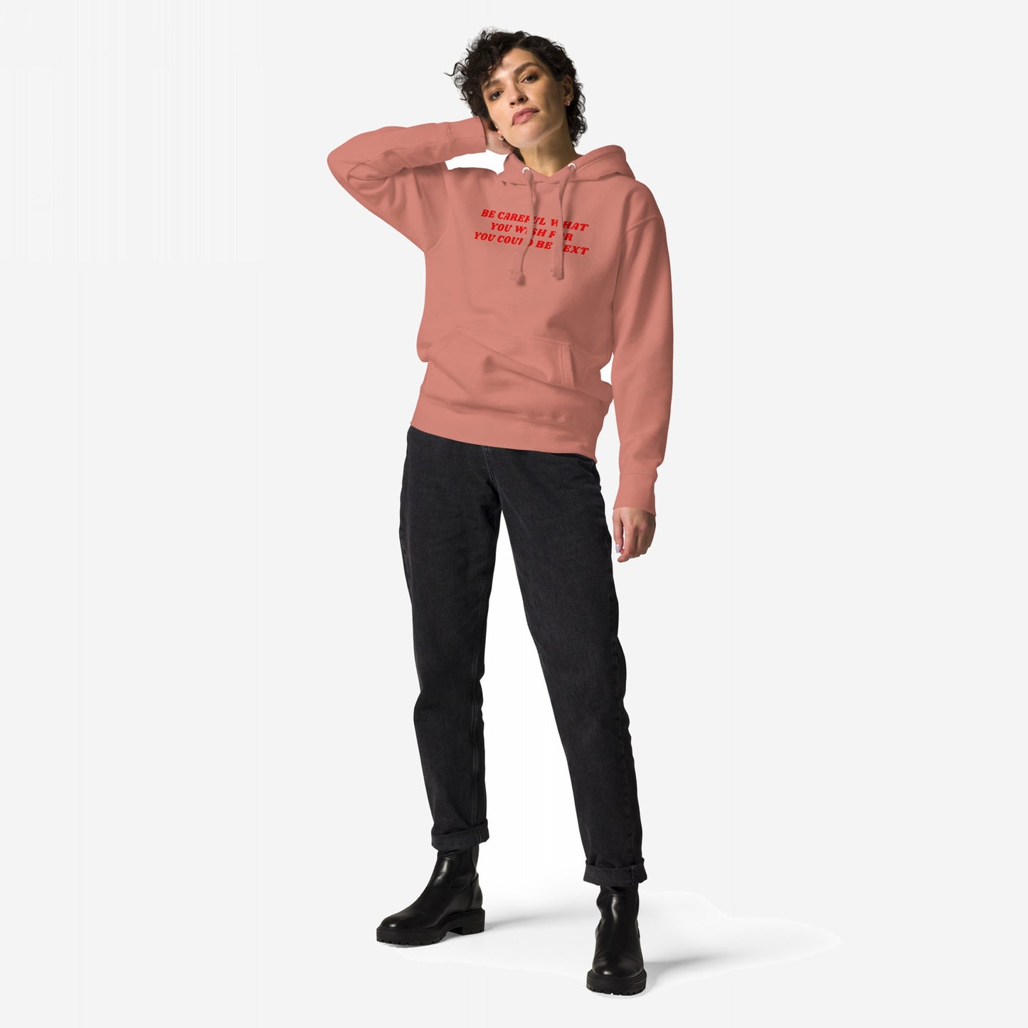Model wearing the Be Careful Hoodie & Sweatshirt, featuring bold red text, BE CAREFUL WHAT YOU WISH FOR YOU COULD BE NEXT, against a rebellious backdrop, paired with black jeans and chunky boots.