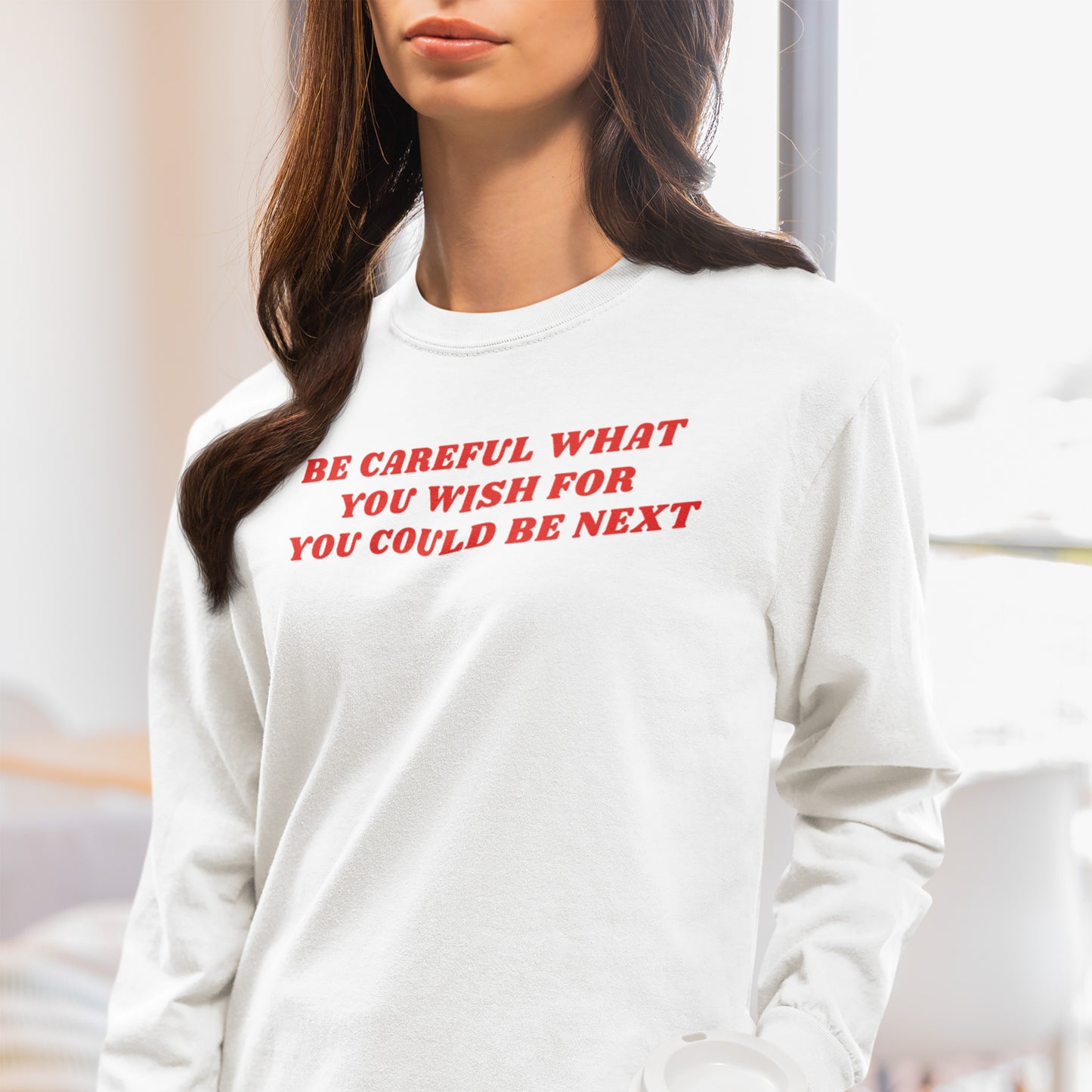 Young woman in a white Be Careful Shirt, featuring bold red text warning against authoritarianism and extremism, holds a white tumbler, embodying a fashion statement for social justice and resistance.