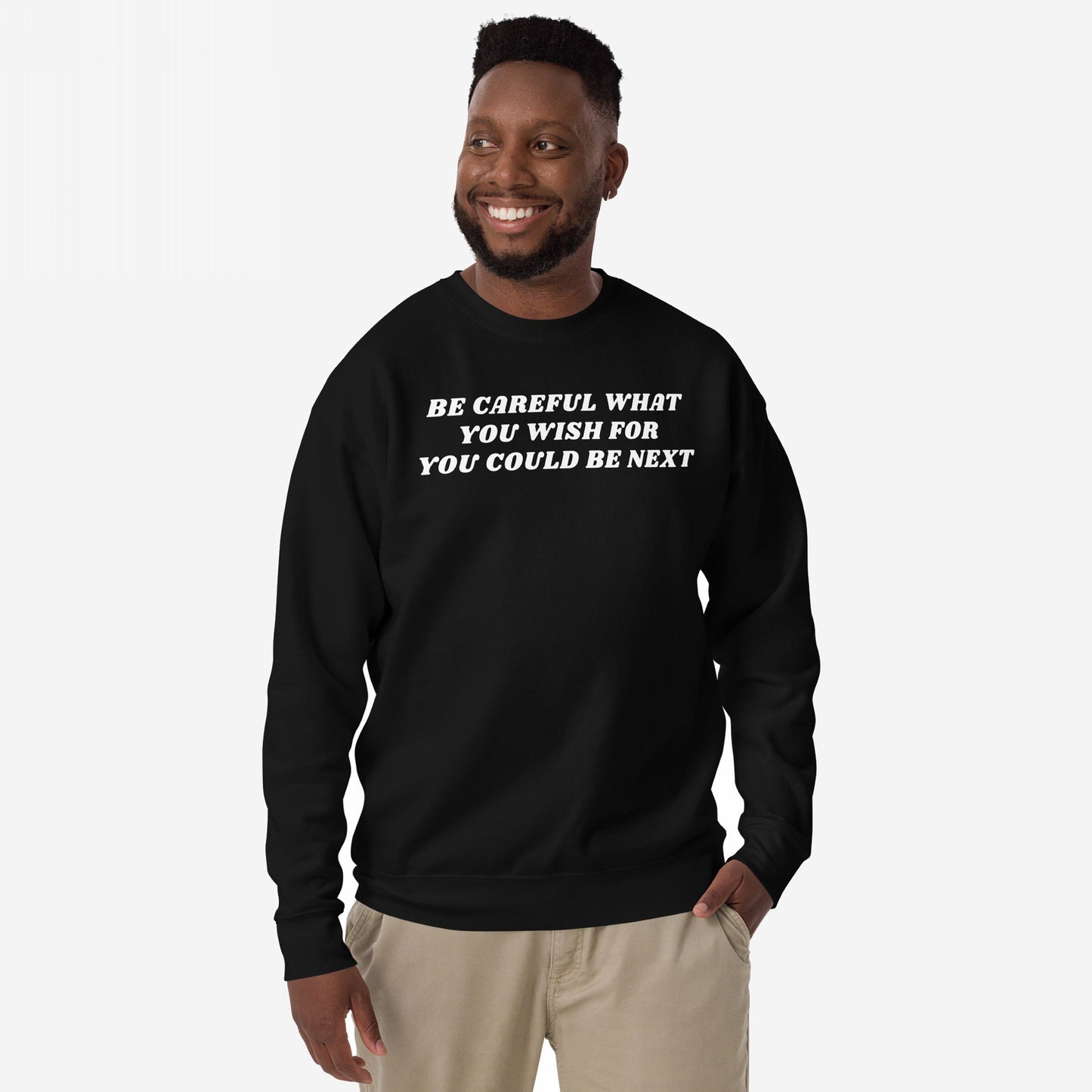A man models the Be Careful Hoodie & Sweatshirt, featuring bold white lettering, embodying a rebellious message against authoritarianism. The sweatshirt is styled casually with light-tan pants.