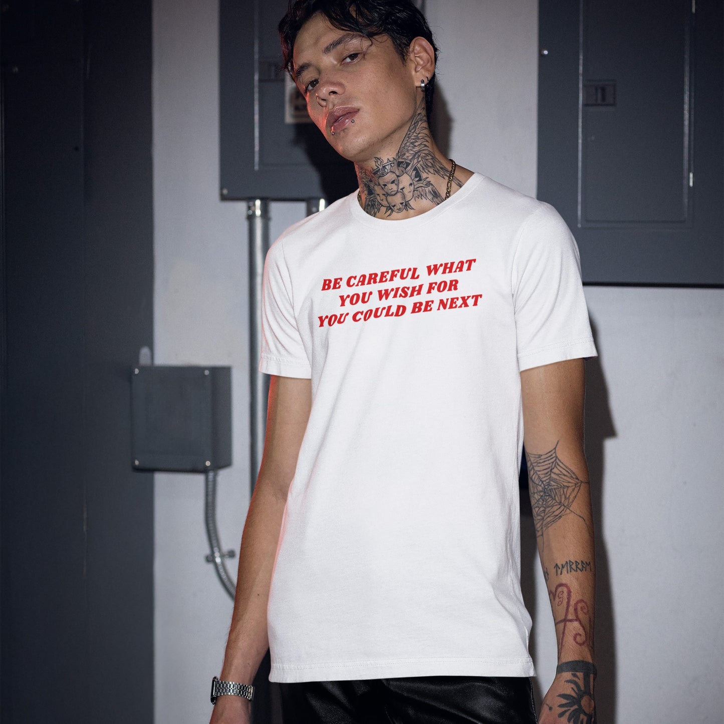 Young individual in a Be Careful T-shirt, featuring bold red text, tattoos, and piercings, embodying rebellious street-wear style. The shirt challenges power structures with its provocative message.