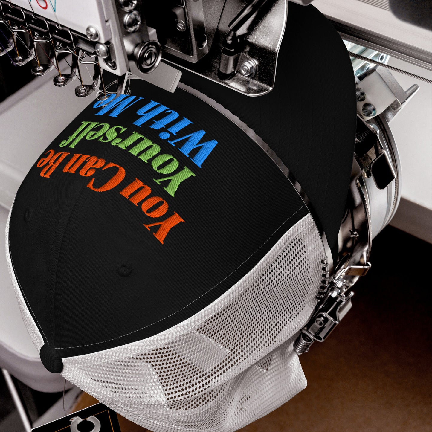 Be Yourself Hat black snapback with colorful embroidered “You Can Be Yourself With Me” text being stitched on sewing machine.