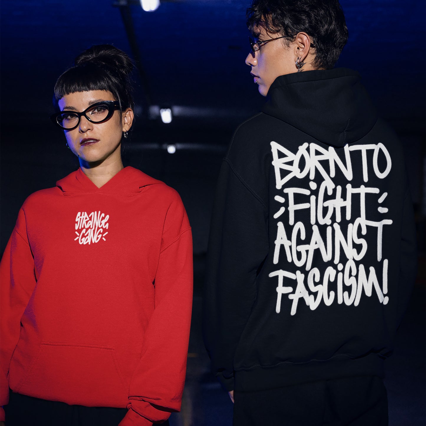 Two young adults in a dim setting showcase the Born To Fight Against Fascism Graffiti Shirt, featuring bold anti-fascist script, embodying protest spirit and supporting the ACLU.
