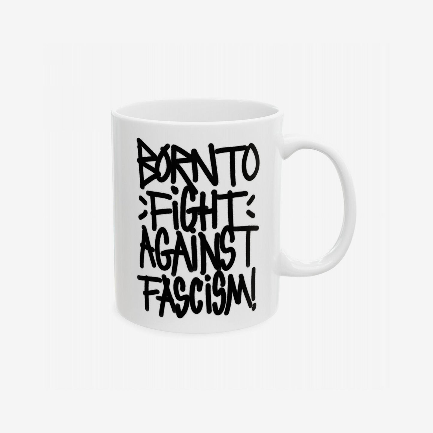 White ceramic mug with bold black lettering reading BORN TO FIGHT AGAINST FASCISM! showcasing a graffiti-style design, symbolizing defiance and activism, printed on both sides.