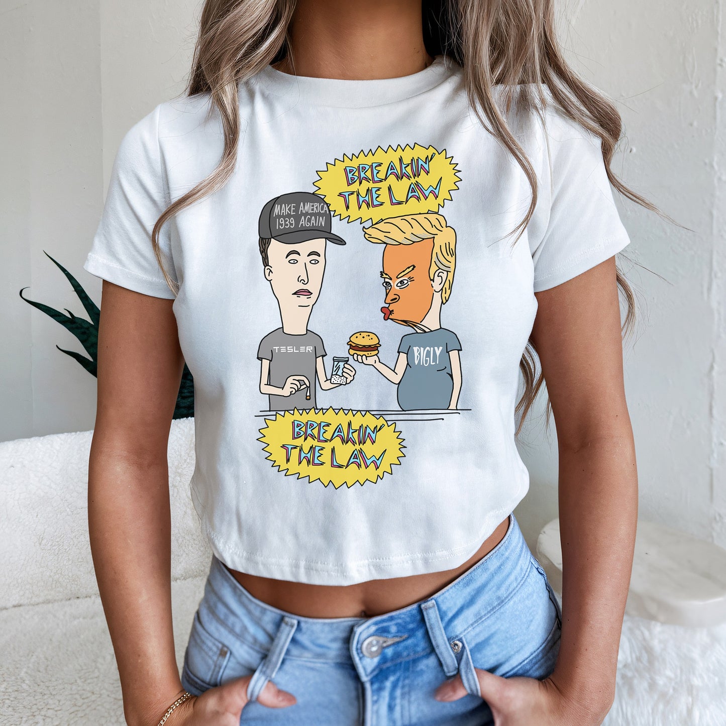 Breakin' The Law Women's Baby Tee features a satirical cartoon of caricatured men behind a counter, humorously parodying notable figures, with slogans in comic bursts, ideal for bold, irreverent expression.