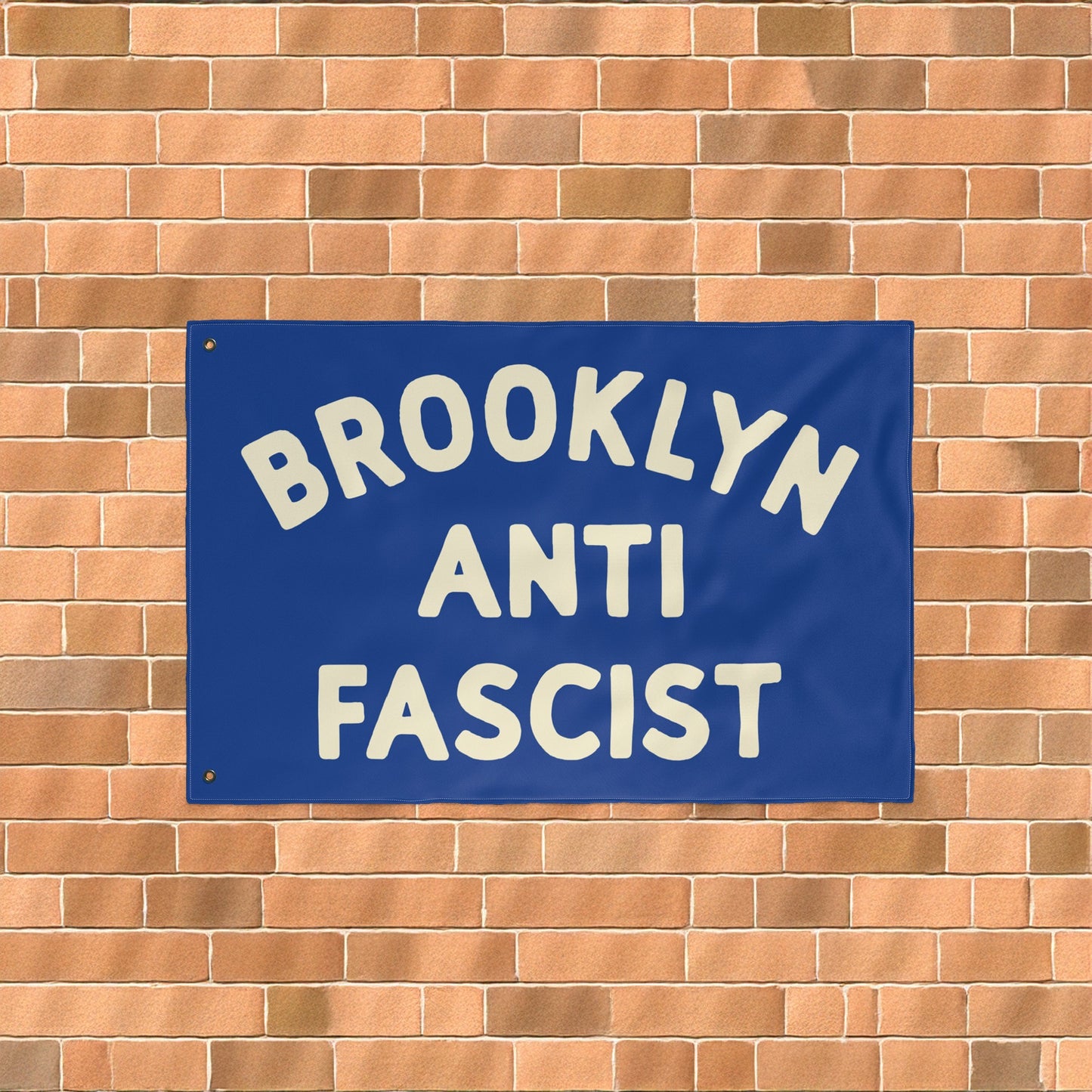 Custom Anti-Fascist Flag displayed on a brick wall, featuring bold off-white block letters reading BROOKLYN ANTI FASCIST. The flag is customizable, showcasing solidarity against fascism and hate.