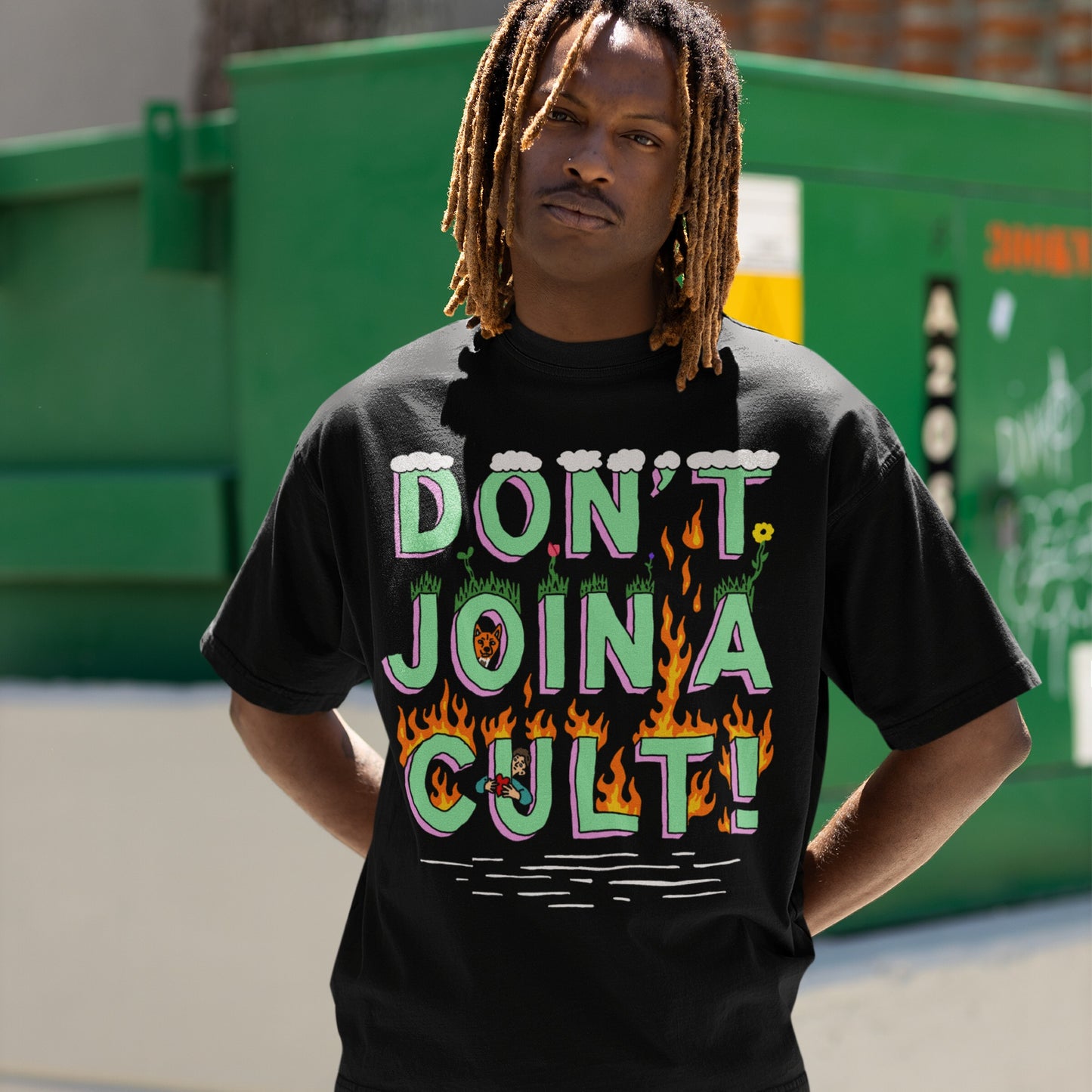 Young person wearing a Don't Join A Cult T-shirt featuring bold cartoon-style text with flames and doodles, standing casually outdoors with hands behind back, exemplifying a statement against authoritarianism.