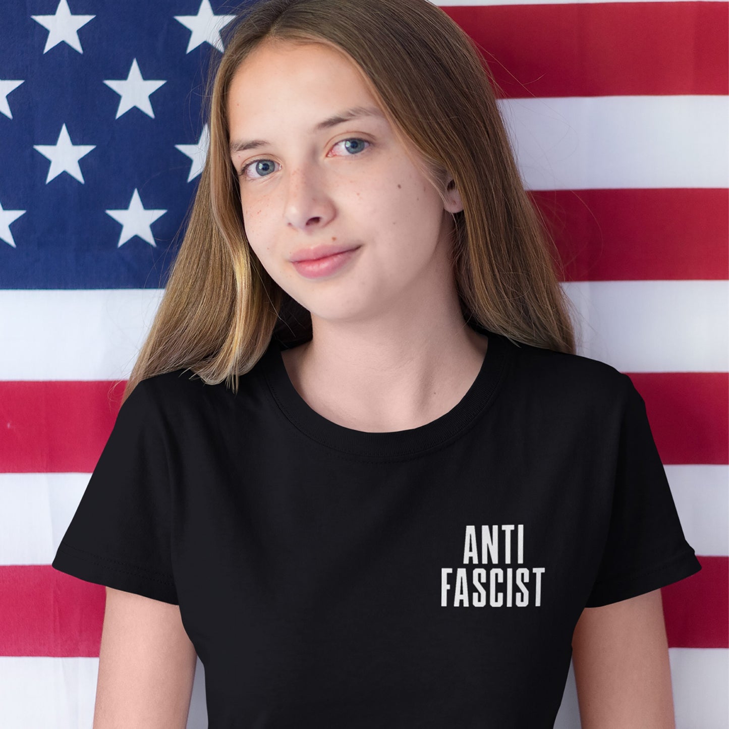 Person in a black ANTI FASCIST T-shirt, titled Fuck 'Em All Back Print T-shirt, standing before an American flag backdrop, embodying a strong anti-fascist message.