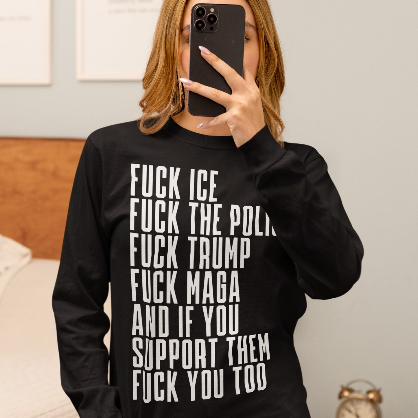 A person takes a mirror selfie wearing the Fuck 'Em All T-shirt, featuring bold, vertical anti-authoritarian statements in white text, covering their face with a smartphone.