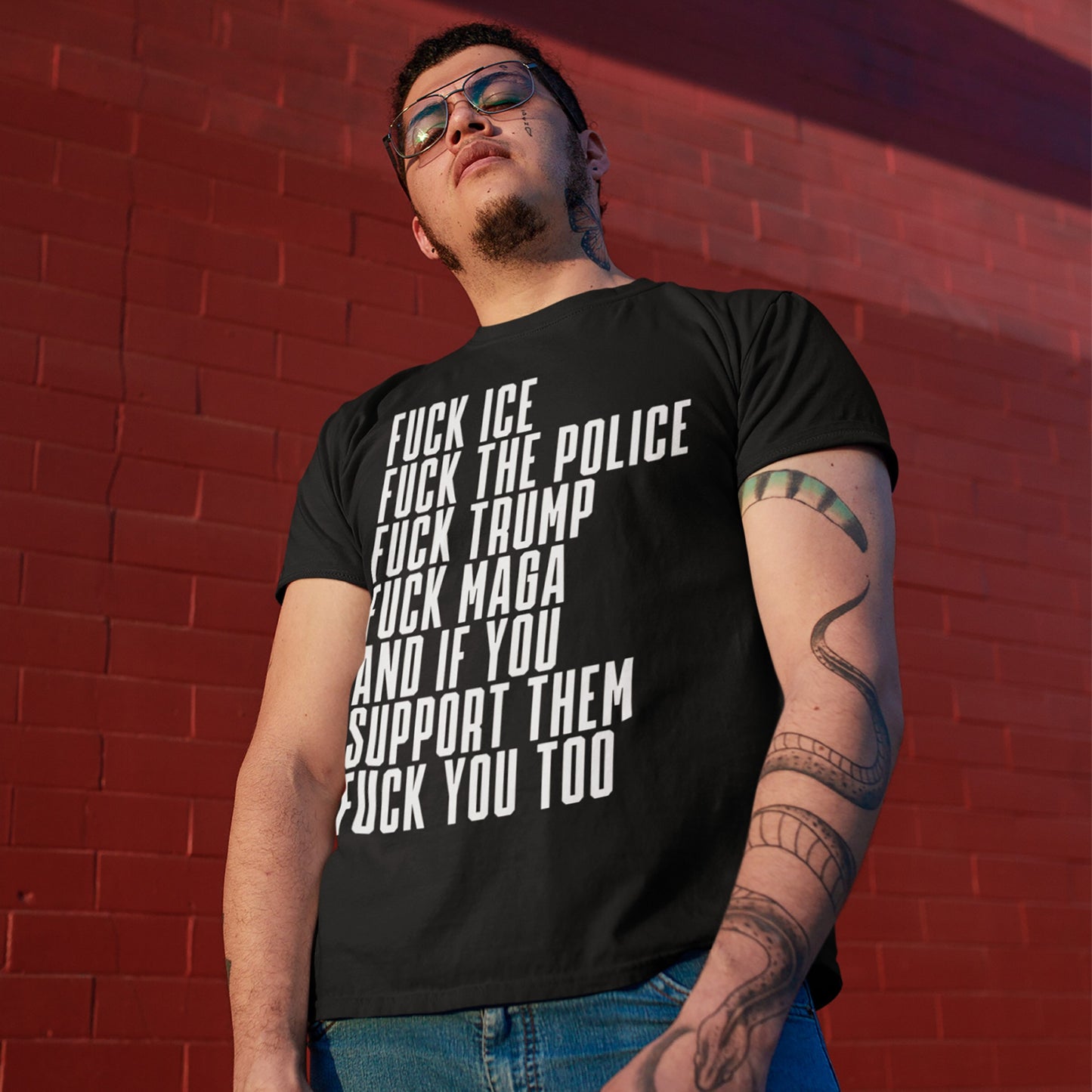 Young person wearing the Fuck 'Em All T-shirt with bold, white, anti-authoritarian statements. The shirt challenges oppressive systems, embodying a rebellious spirit. Visible sleeve tattoo with a snake motif on forearm.