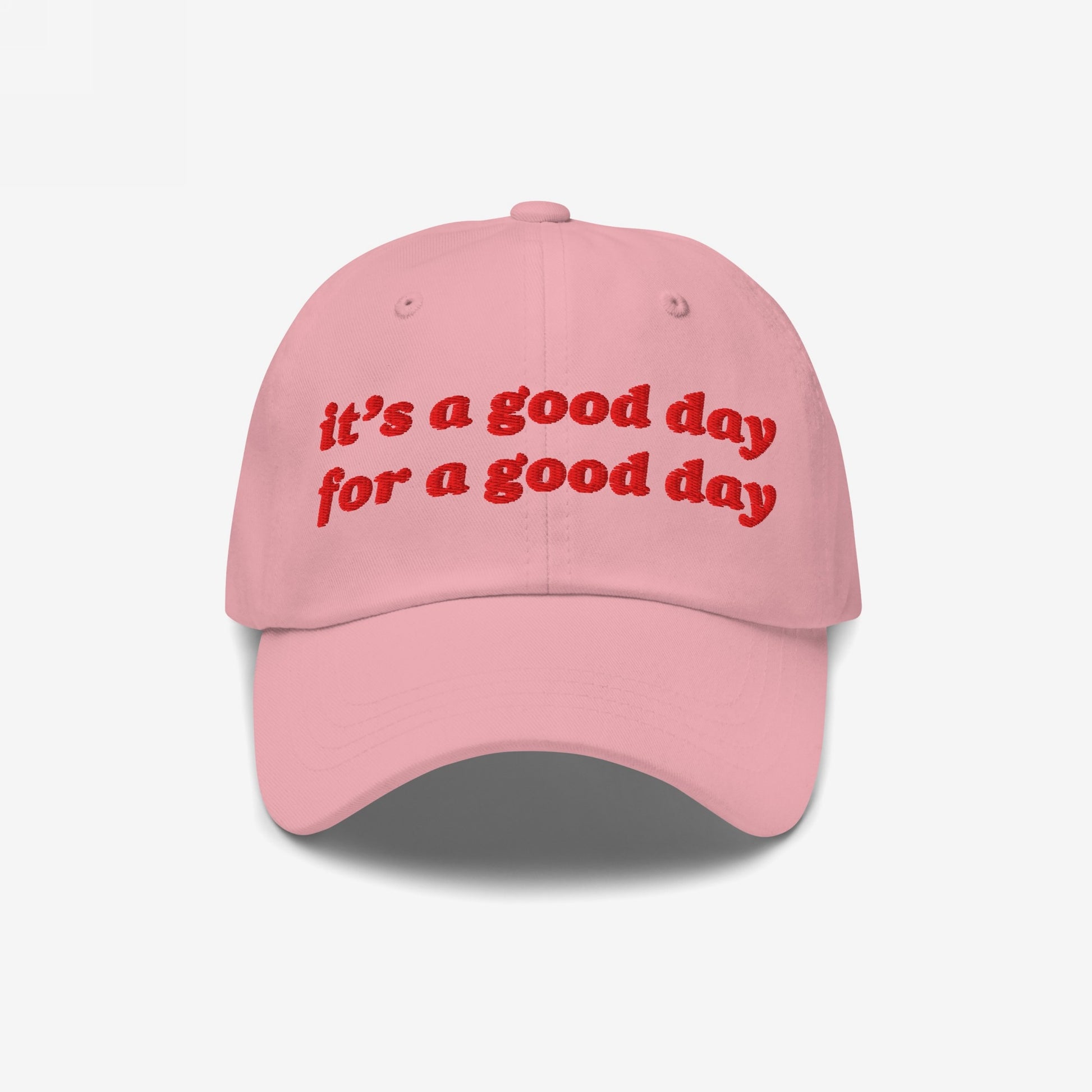 The Good Day Hat features uplifting red embroidery stating, “it’s a good day for a good day,” on a light pink baseball cap, embodying positive energy and mental health advocacy.