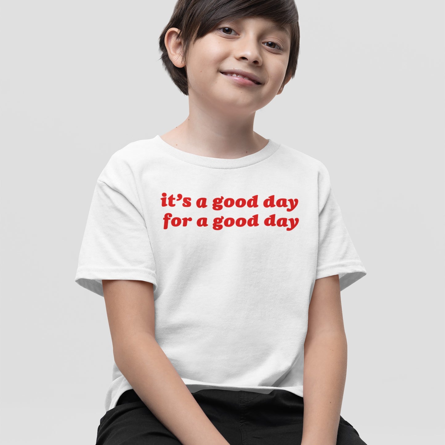 Young boy wearing a Good Day T-shirt with red bold text, it's a good day for a good day, projecting vintage optimism and positive vibes, set against a light-gray background.