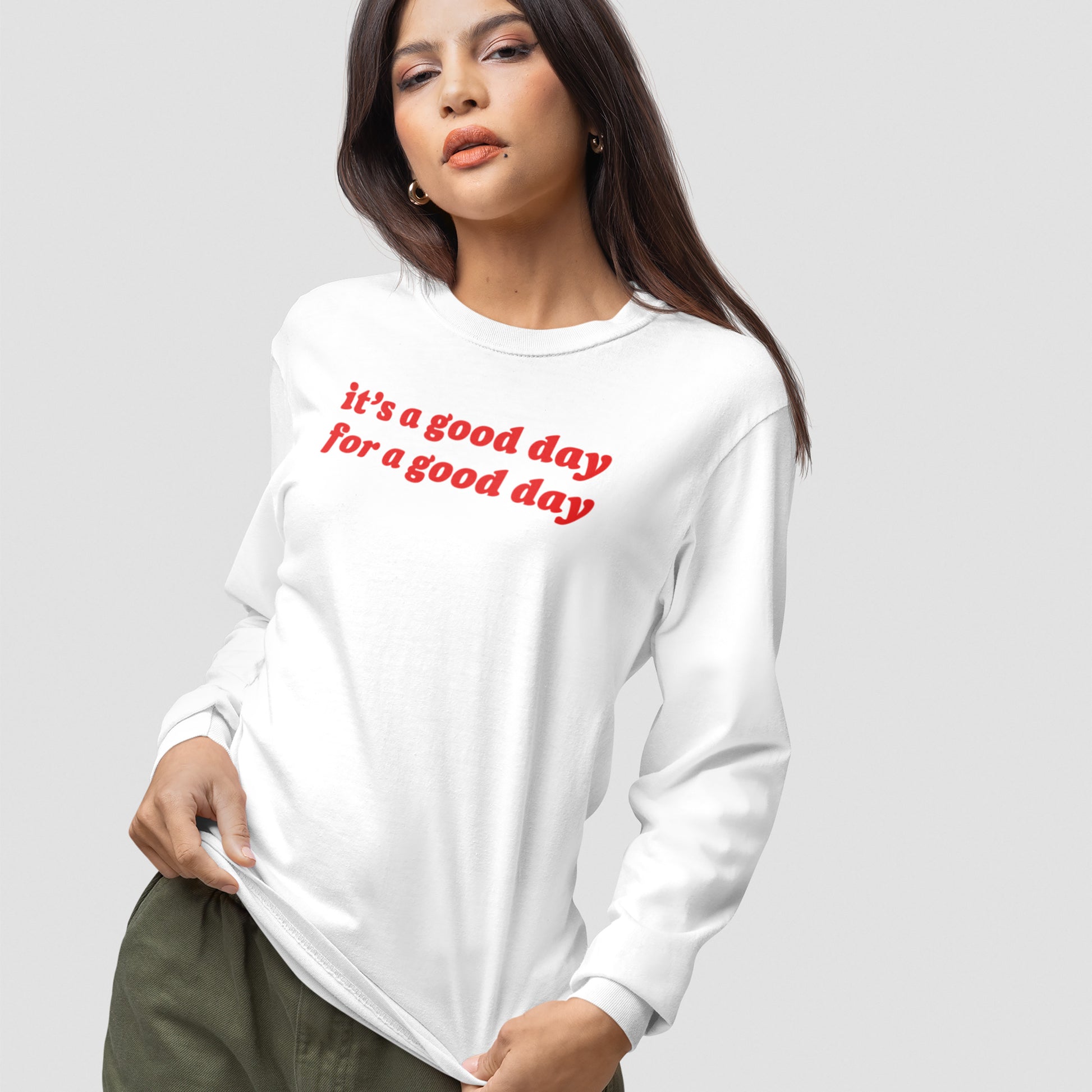 Model wearing the Good Day Shirt, featuring red italic text it’s a good day for a good day on a white long-sleeve, paired with olive-green pants, embodying positivity and vintage vibes.