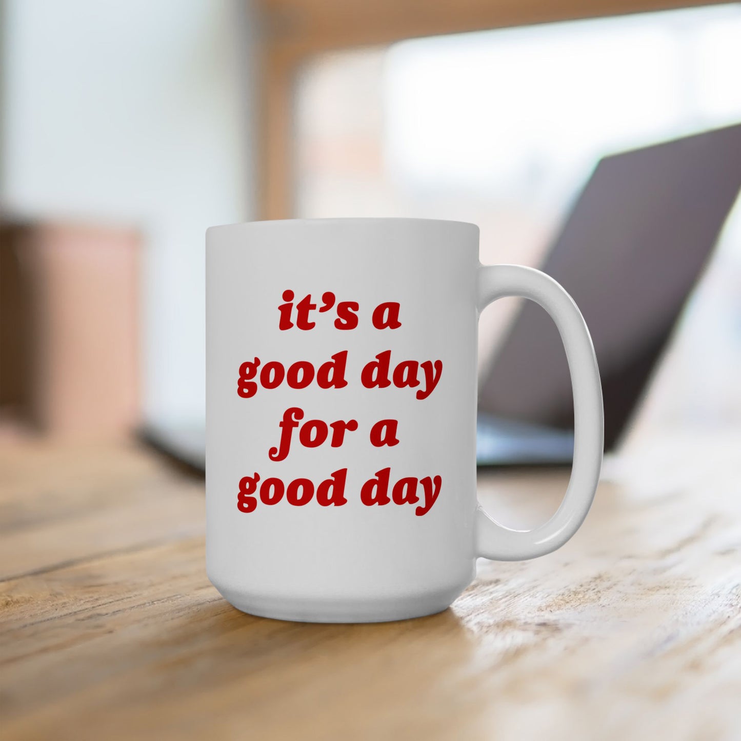 White ceramic Good Day Mug with bold red text it’s a good day for a good day, sits on a wooden desk near an open laptop, embodying positivity for your morning routine.