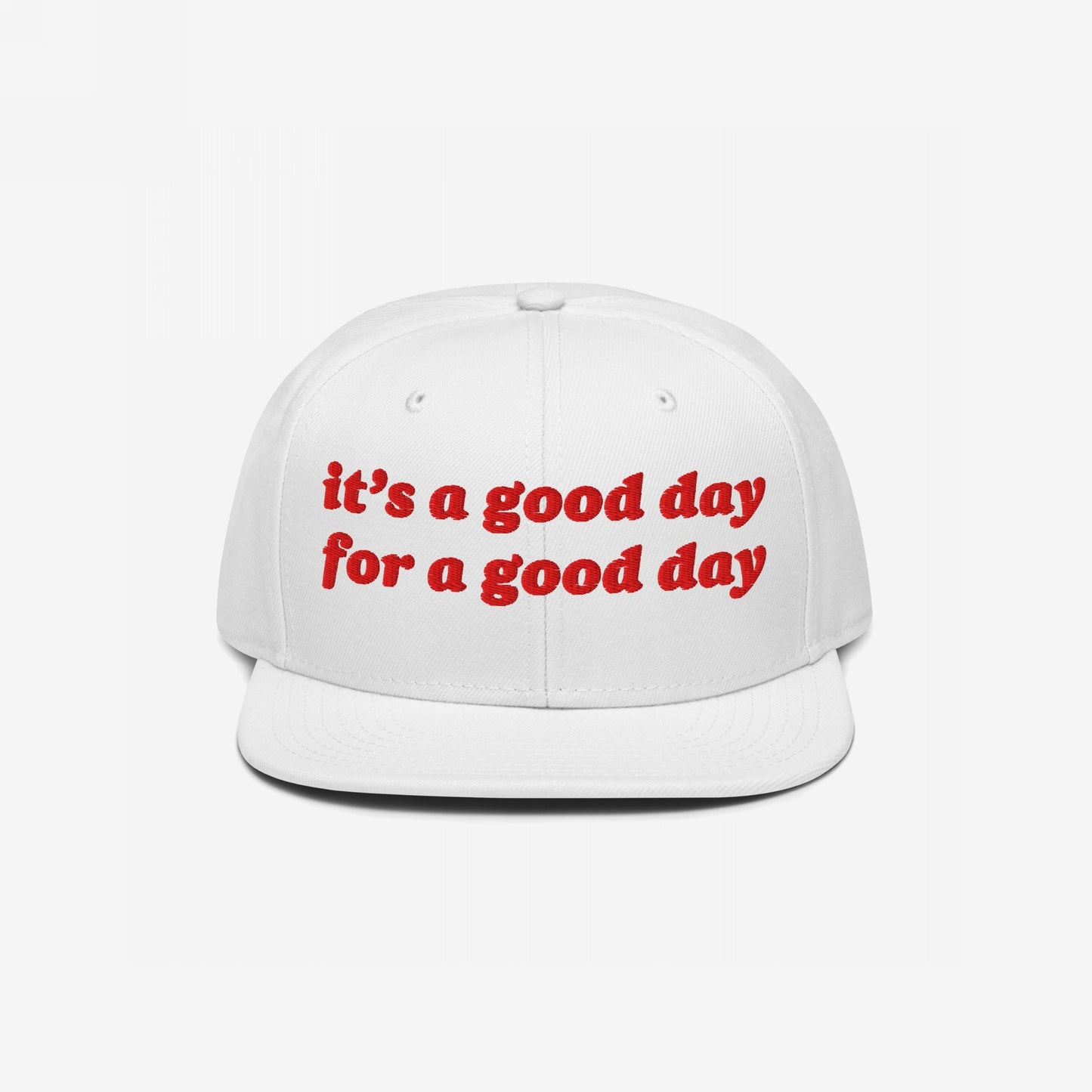 The Good Day Hat features a white, flat-brimmed baseball cap with red, retro-style embroidery stating “it’s a good day for a good day,” embodying optimism and support for mental health advocacy.