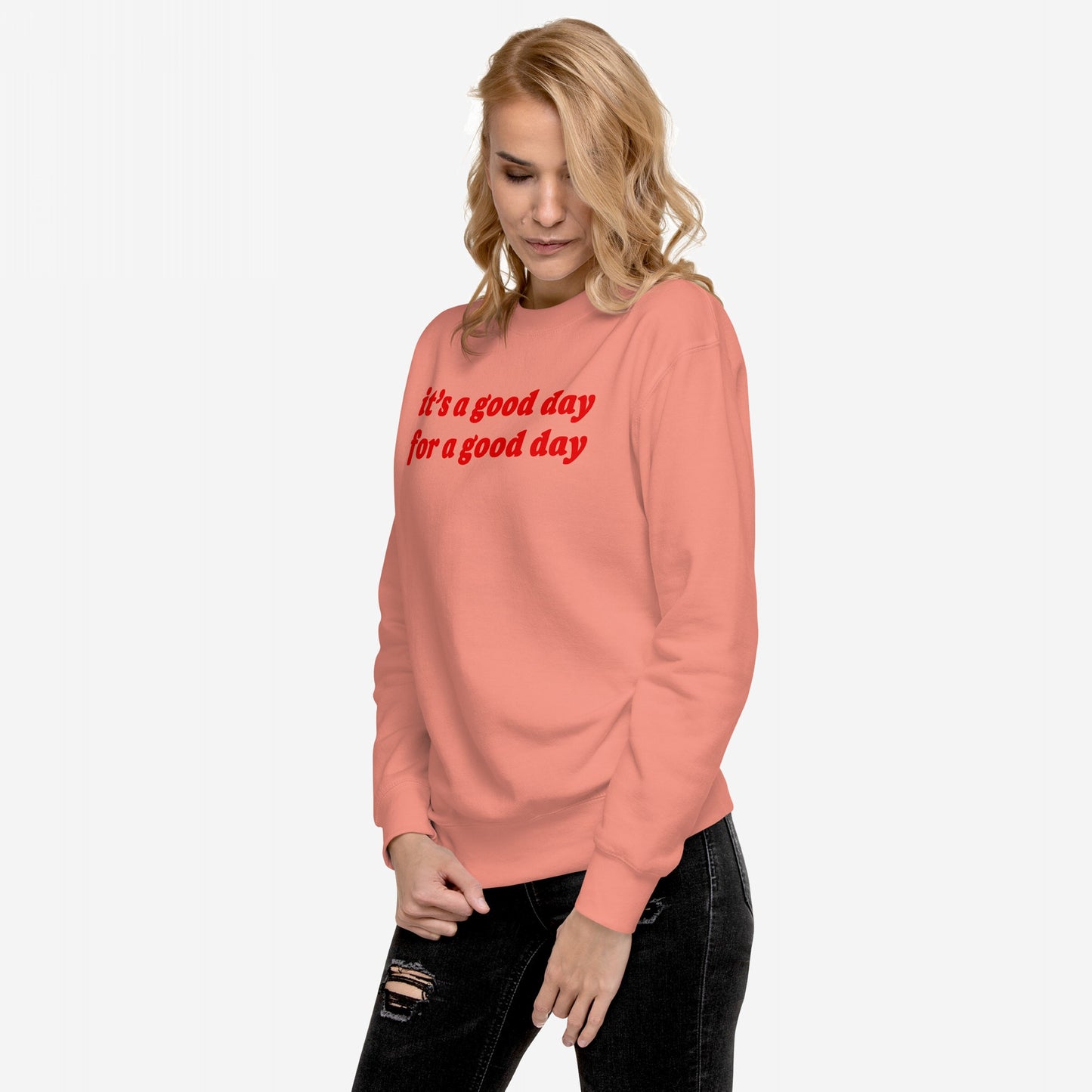 Woman in a muted coral Good Day Hoodie & Sweatshirt with it’s a good day for a good day in bold red script, paired with black distressed jeans, exuding warmth and positivity.