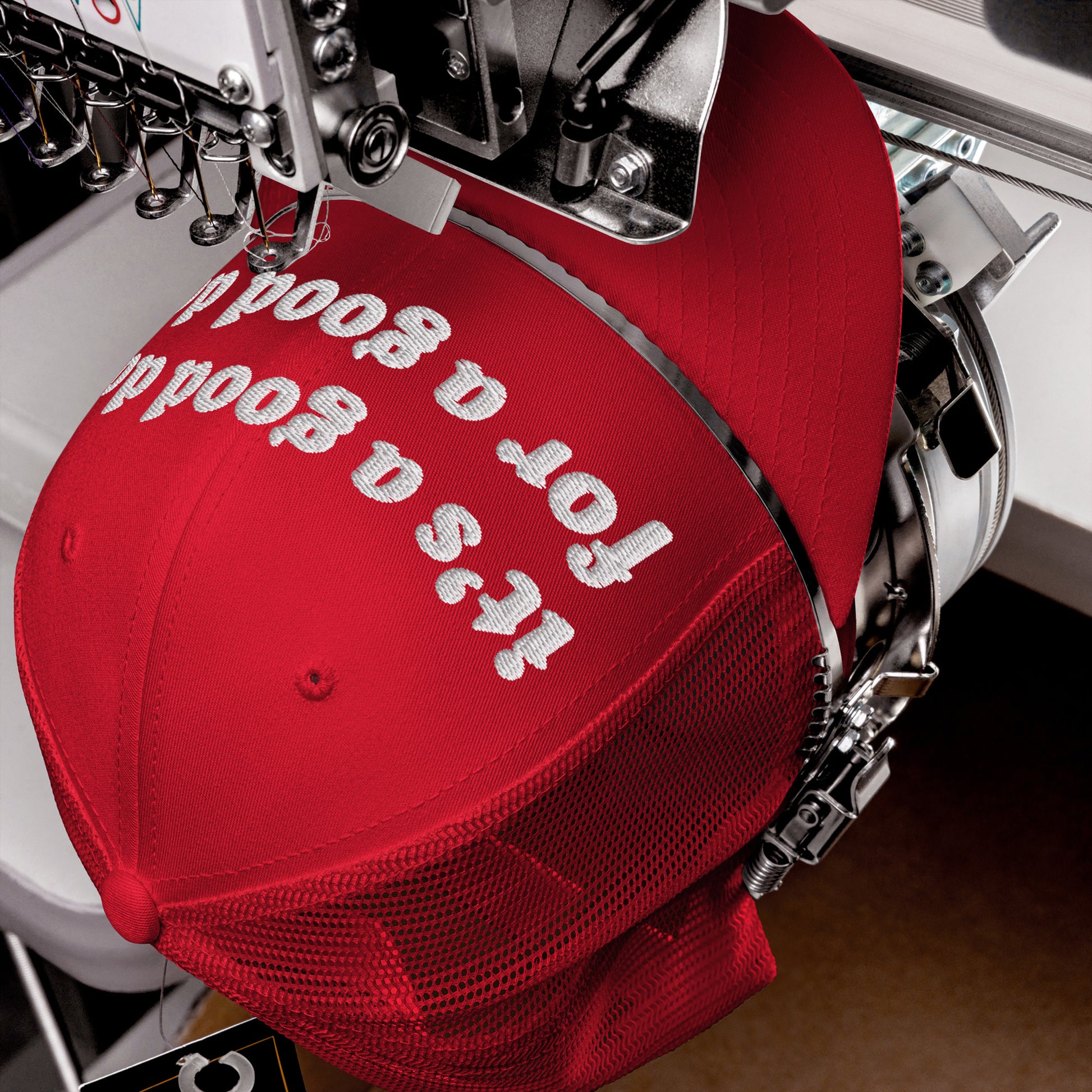 Good Day Hat in a red mesh-back design being embroidered with white text on an industrial machine, showcasing a positive message ideal for mental health advocacy and spreading kindness.