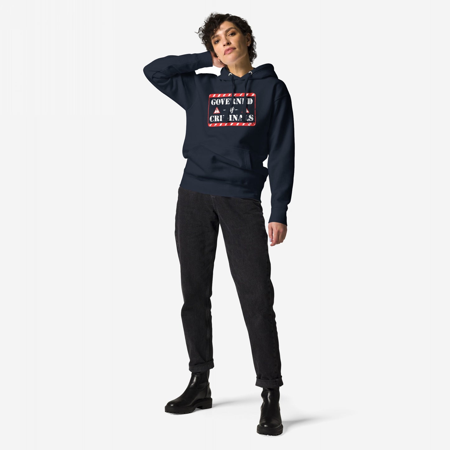 Woman models the Governed By Criminals Hoodie, featuring a bold graphic with GOVERNMENT IS 4 CRIMINALS text, paired with black jeans and lace-up boots, embodying a stance against corruption.
