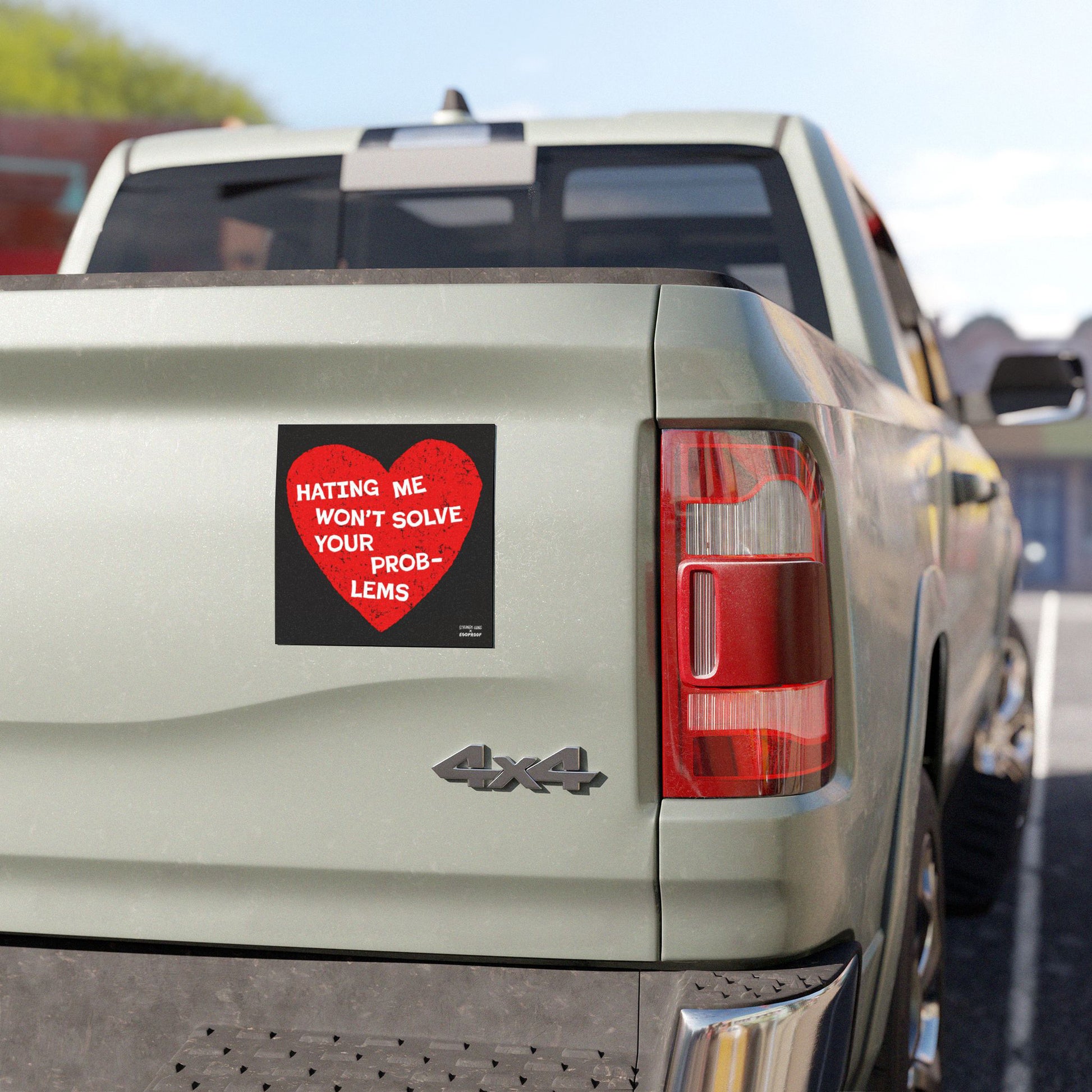 No Hate Sticker & Magnet on a light-green pickup's tailgate, featuring a distressed red heart and slogan advocating for human rights and inclusion. Part of taillight and bumper visible.