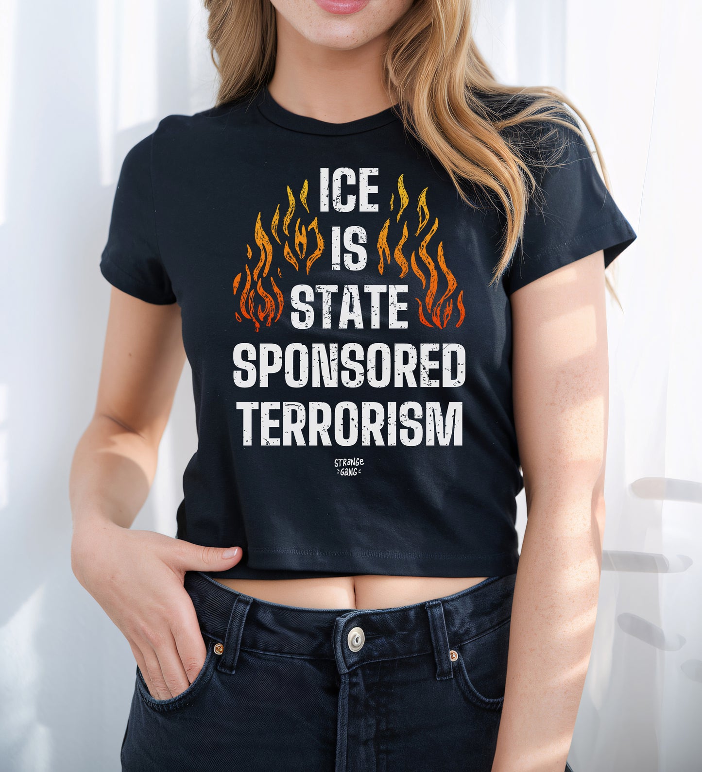 Young person models the ICE Is State Sponsored Terrorism Women's Baby Tee, featuring bold flame graphics and impactful message, ideal for expressing resistance and supporting immigrant rights.
