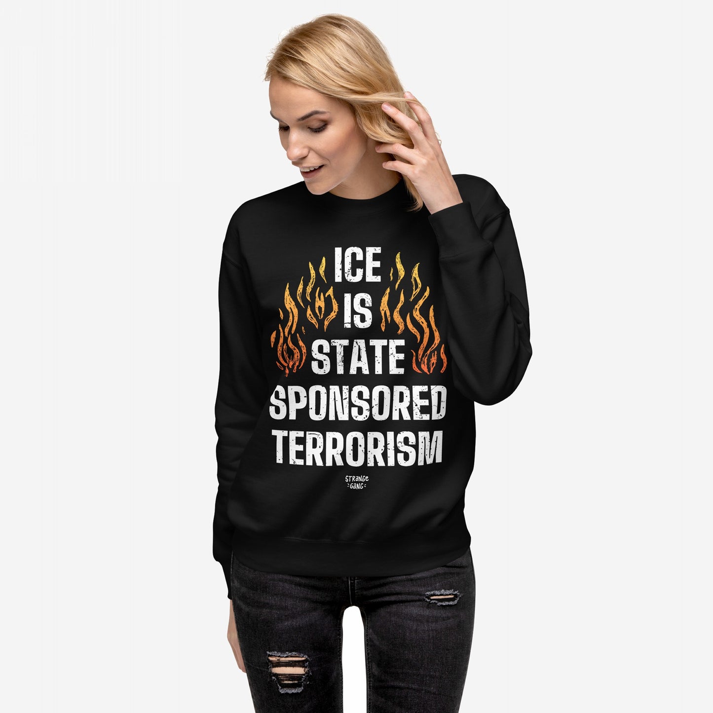 Woman wearing ICE Is State Sponsored Terrorism Hoodie & Sweatshirt, featuring bold flame graphic and powerful slogan. She touches her hair, embodying a stance for immigrant justice and resistance.