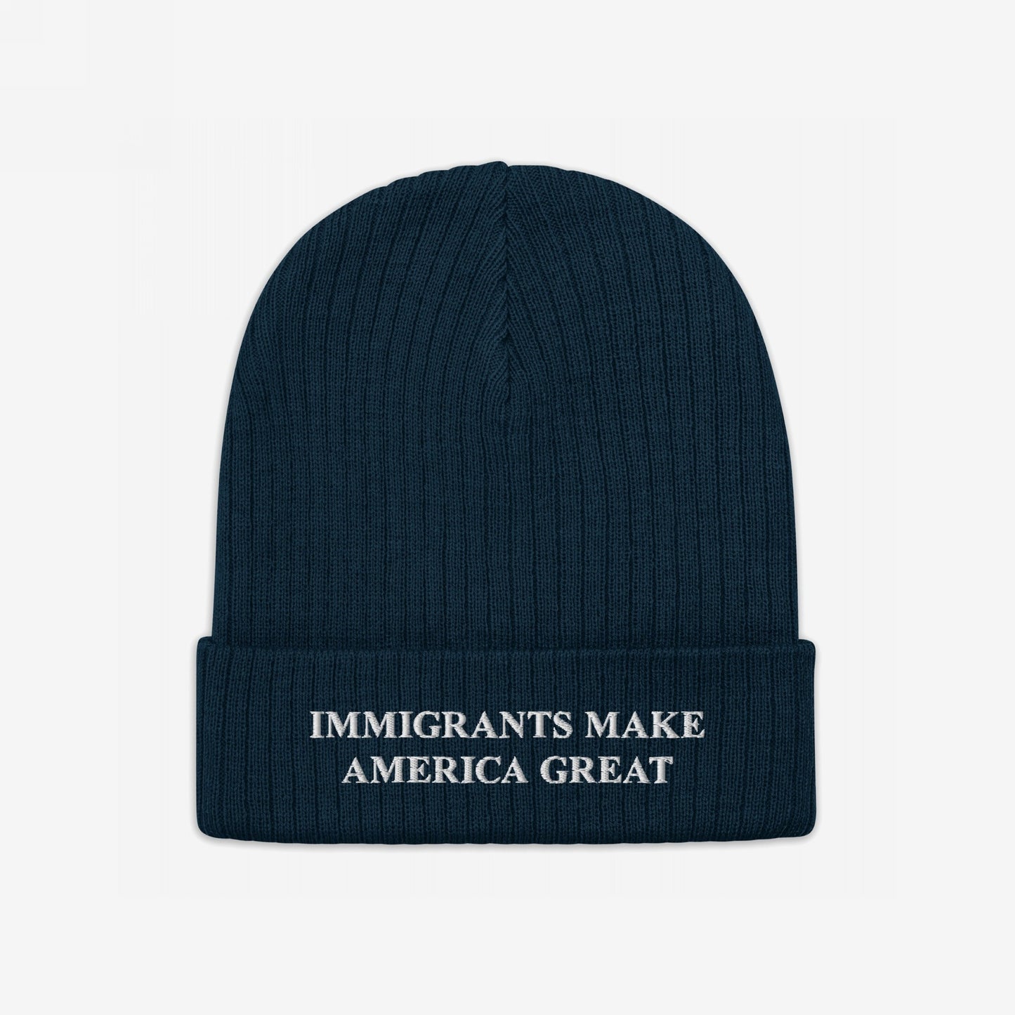 Dark-blue rib-knit beanie hat with folded cuff, featuring bold white embroidery: “IMMIGRANTS MAKE AMERICA GREAT.” Designed for advocates of equality and immigrant rights, supporting Amnesty International.
