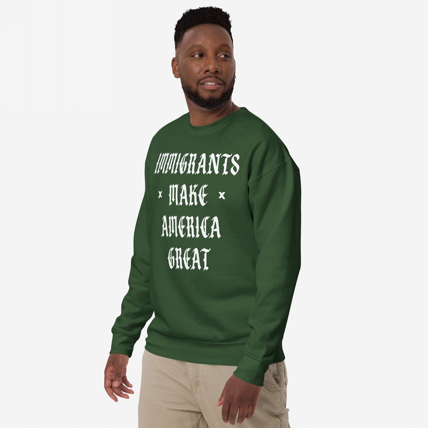 Man wears Immigrants Make America Great Sweatshirt with white Old English lettering, expressing immigrant pride and power. Paired with khaki pants, this piece supports equality and challenges nationalism.