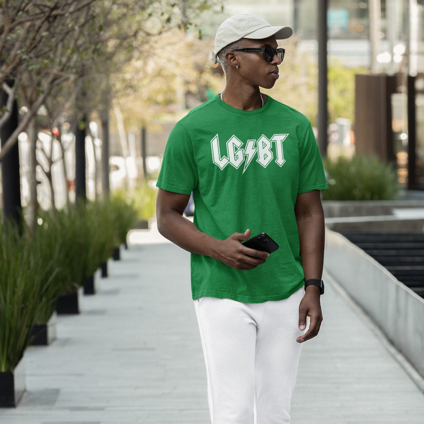 Young man wearing the LGBTQ Rocks T-shirt with a bold rock-band logo, styled for pride and visibility, walks along a city sidewalk, holding a smartphone and exuding confidence and solidarity.