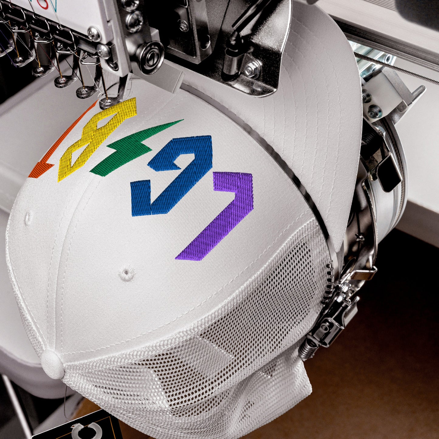 White LGBTQ Rocks Hat with rainbow embroidery being stitched on a mesh trucker hat showcasing pride and rock style.