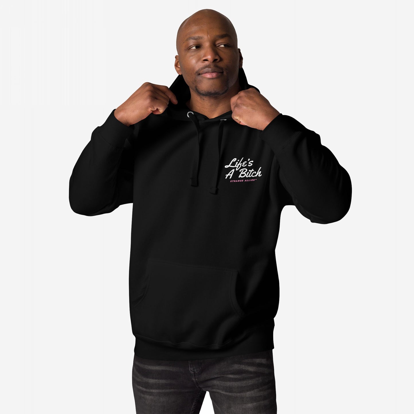 Life's A Bitch Hoodie & Sweatshirt features a man adjusting its hood, displaying a bold slogan on the chest. This cozy garment embodies unapologetic realism with a kangaroo pocket and drawstrings.