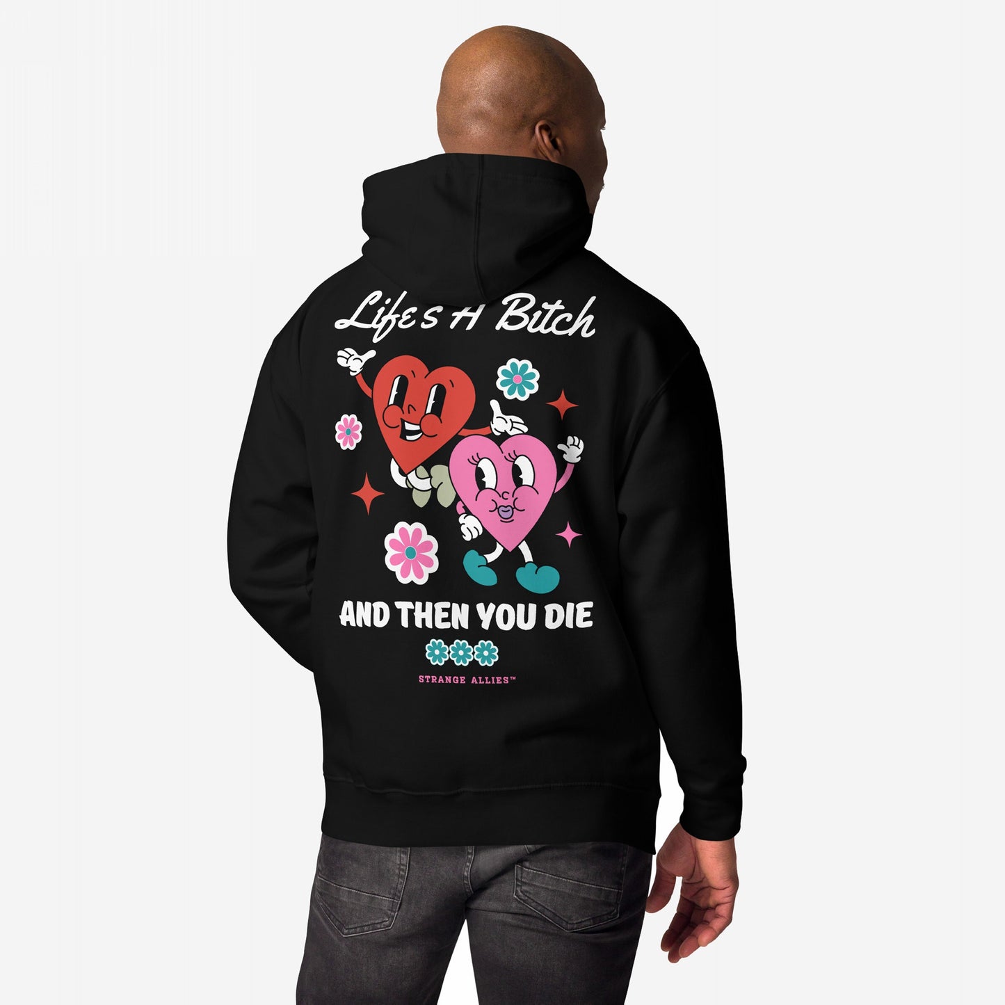 A person wears the Life's A Bitch Hoodie, featuring cartoon hearts and flowers with the slogan “Life’s a Bitch, And Then You Die,” embracing unapologetic realism, trademarked by Strange Allies.