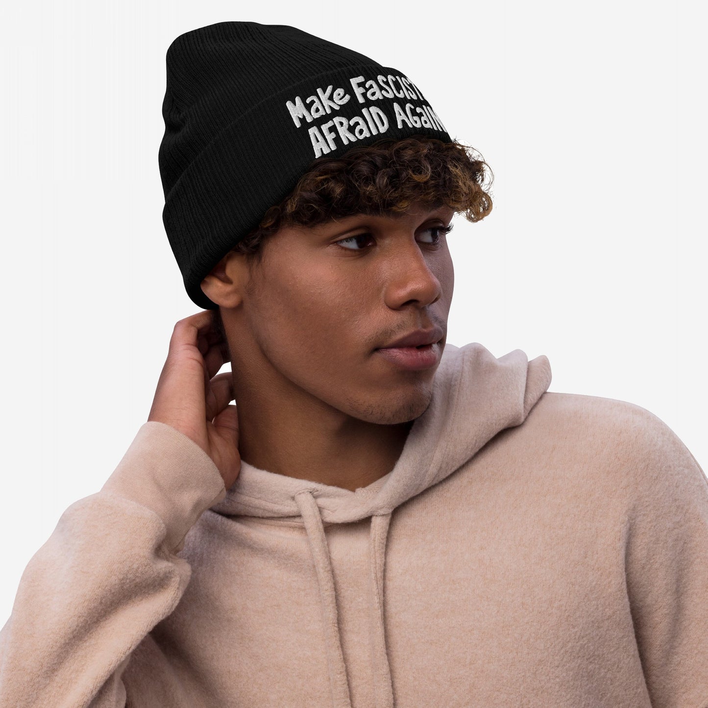 Young man in a pale-beige hoodie wears a black Make Fascists Afraid Again knit beanie, featuring bold, hand-drawn lettering, embodying a spirit of unapologetic resistance.