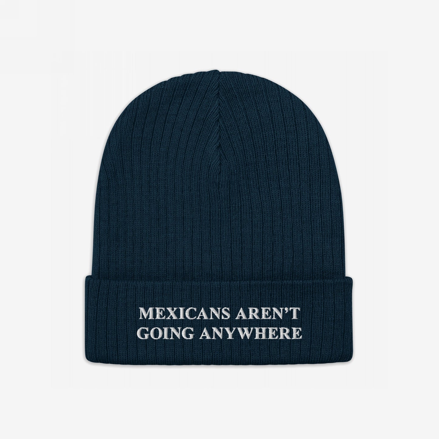 Dark navy-blue knit beanie with “MEXICANS AREN’T GOING ANYWHERE” embroidered in white, embodying pride and resistance against racism and nationalism.