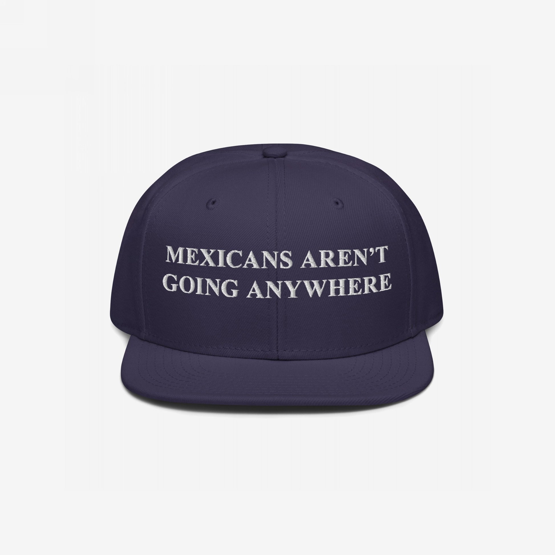 Navy snap-back cap with white embroidered Mexicans Aren’t Going Anywhere text, embodying pride and resistance against racism, available in multiple styles. Supports Immigrant Legal Resource Center.