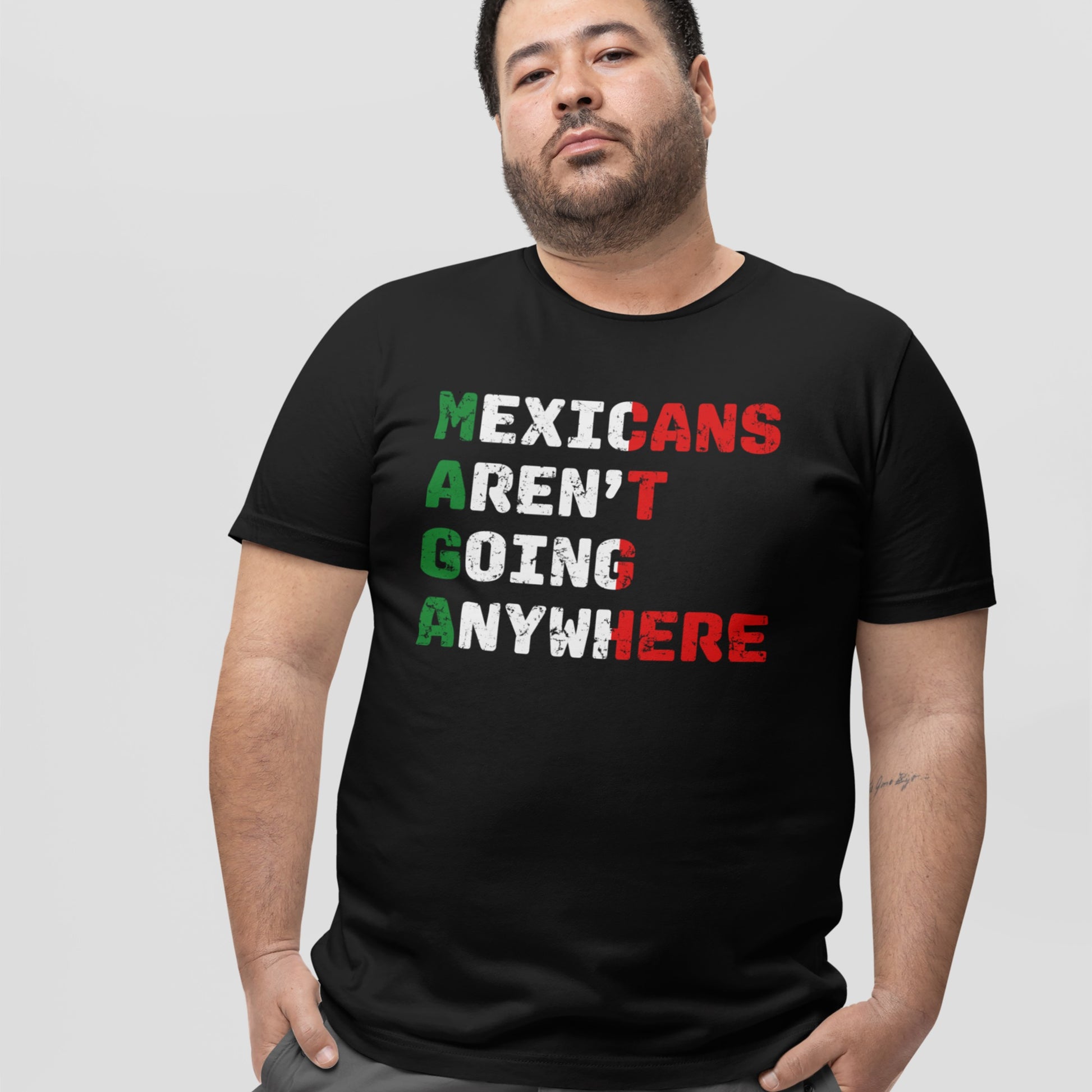 Man wearing Mexicans Aren’t Going Anywhere Shirt, featuring the phrase in bold letters with MAGA highlighted in Mexican flag colors, symbolizing defiance and pride against exclusion.